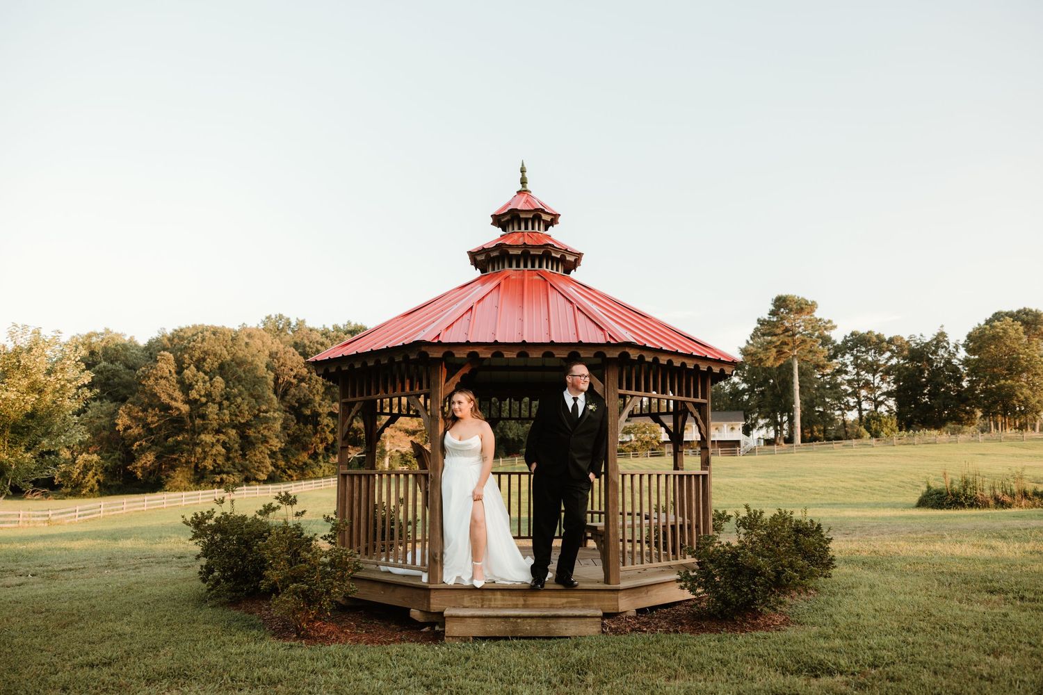 Beautiful outdoor wedding ceremony in a rustic octagonal gazebo with red roof surrounded by green landscape.