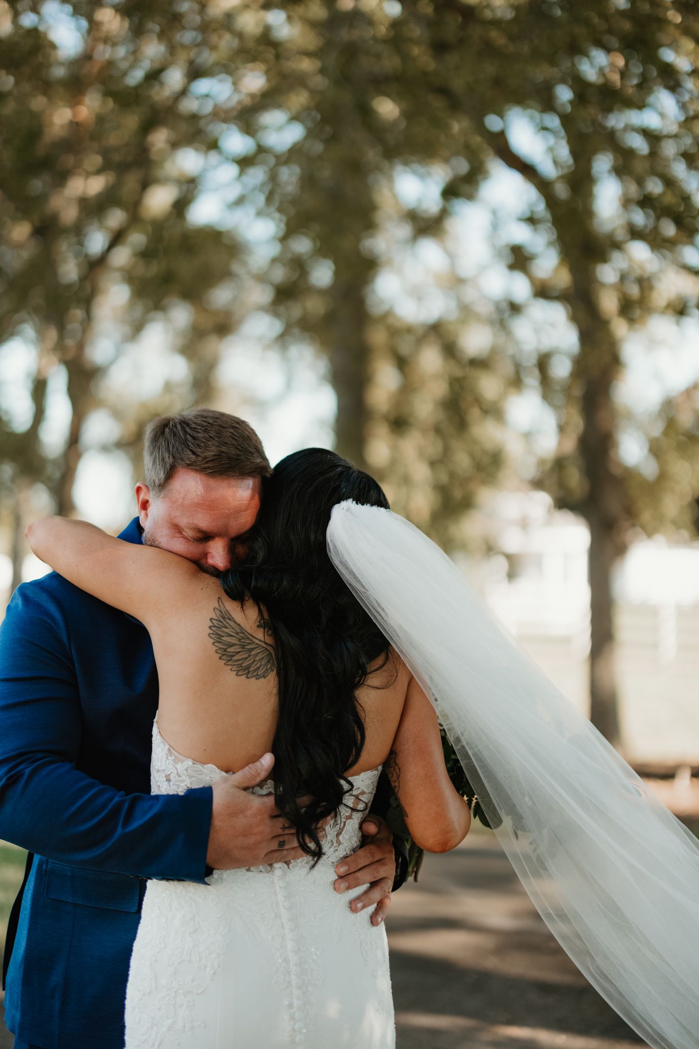 A romantic wedding couple sharing tender kisses in a dreamy outdoor setting with trees and natural lighting.