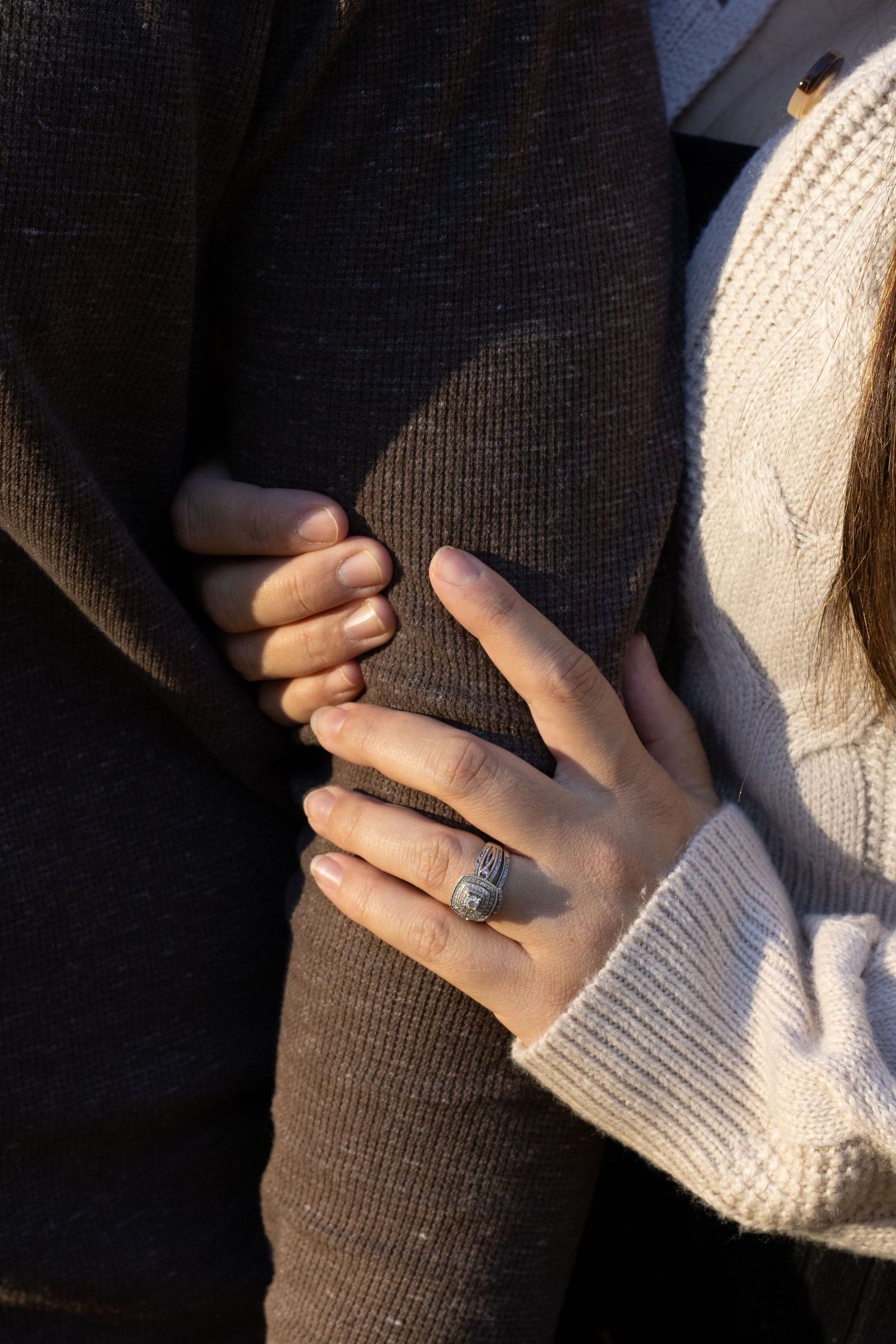 a picture showcasing a ring with her arm wrapped around her husband's arm. the picture is warm and inviting