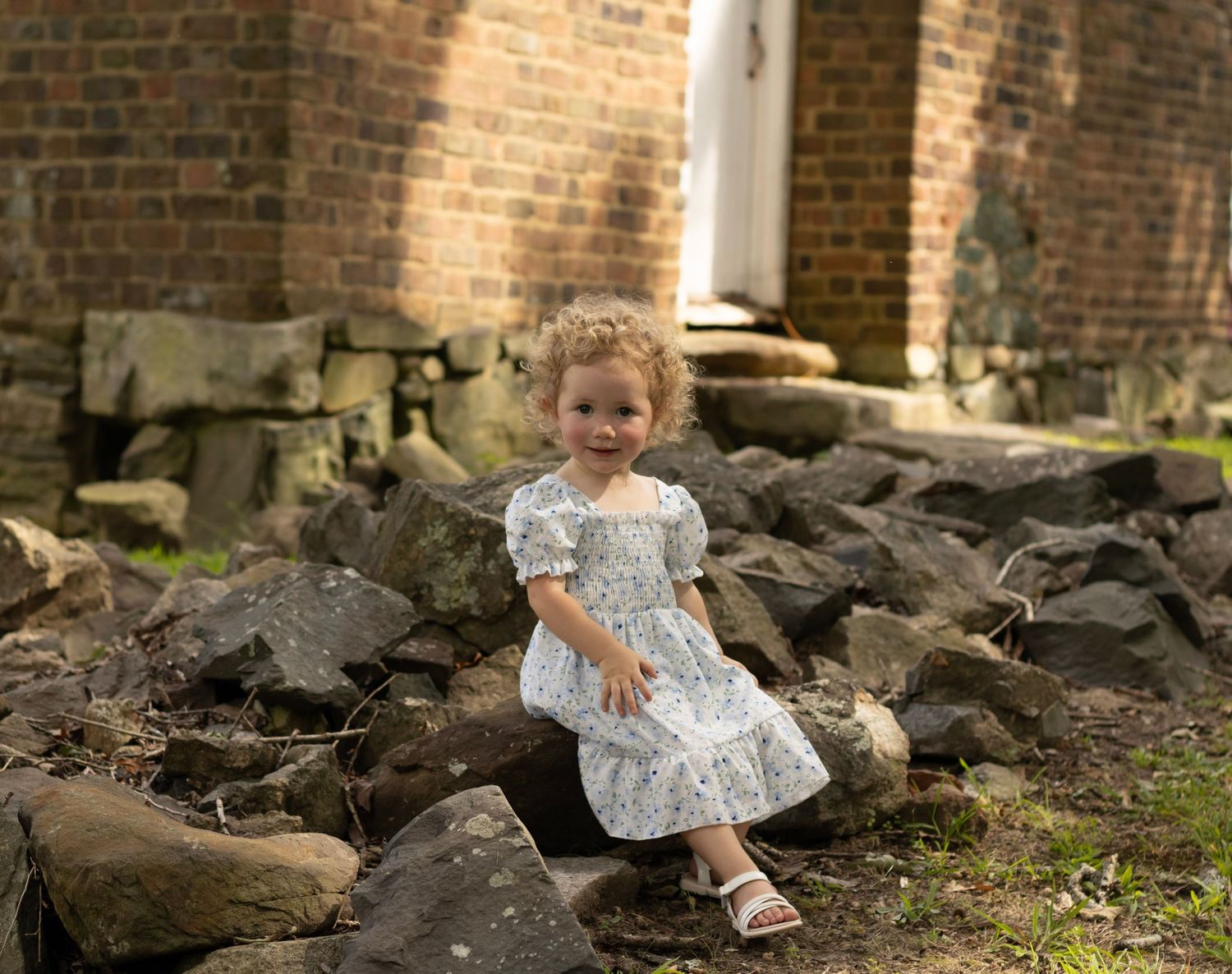 A picture in color showing a toddler sitting on rocks giving a huge smile to the camera. this is a little house on the Perrie inspiration