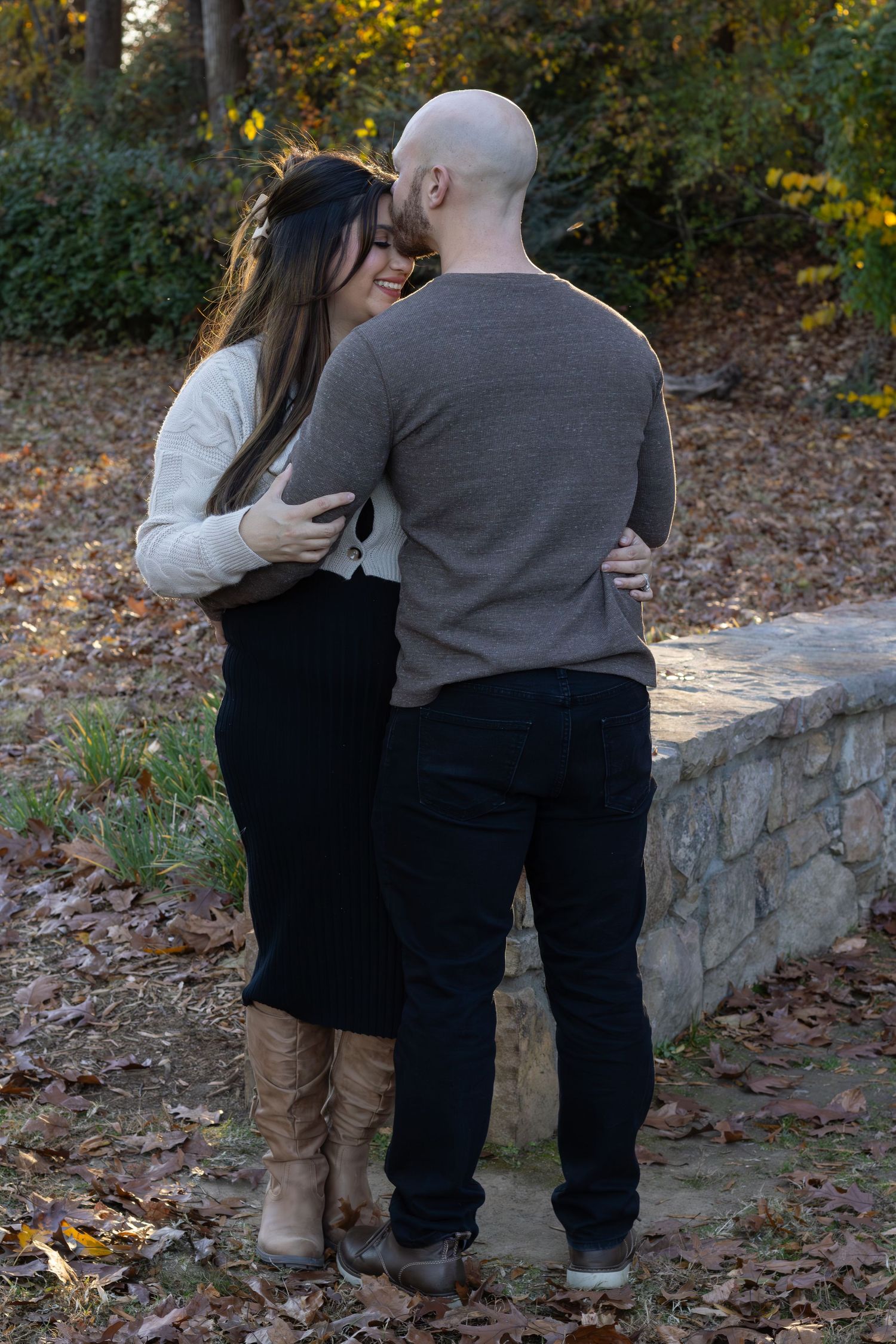 A sweet couple with an intimate pose. The background is lit with the sun. The models are placed in the center of the frame with fall leaves.