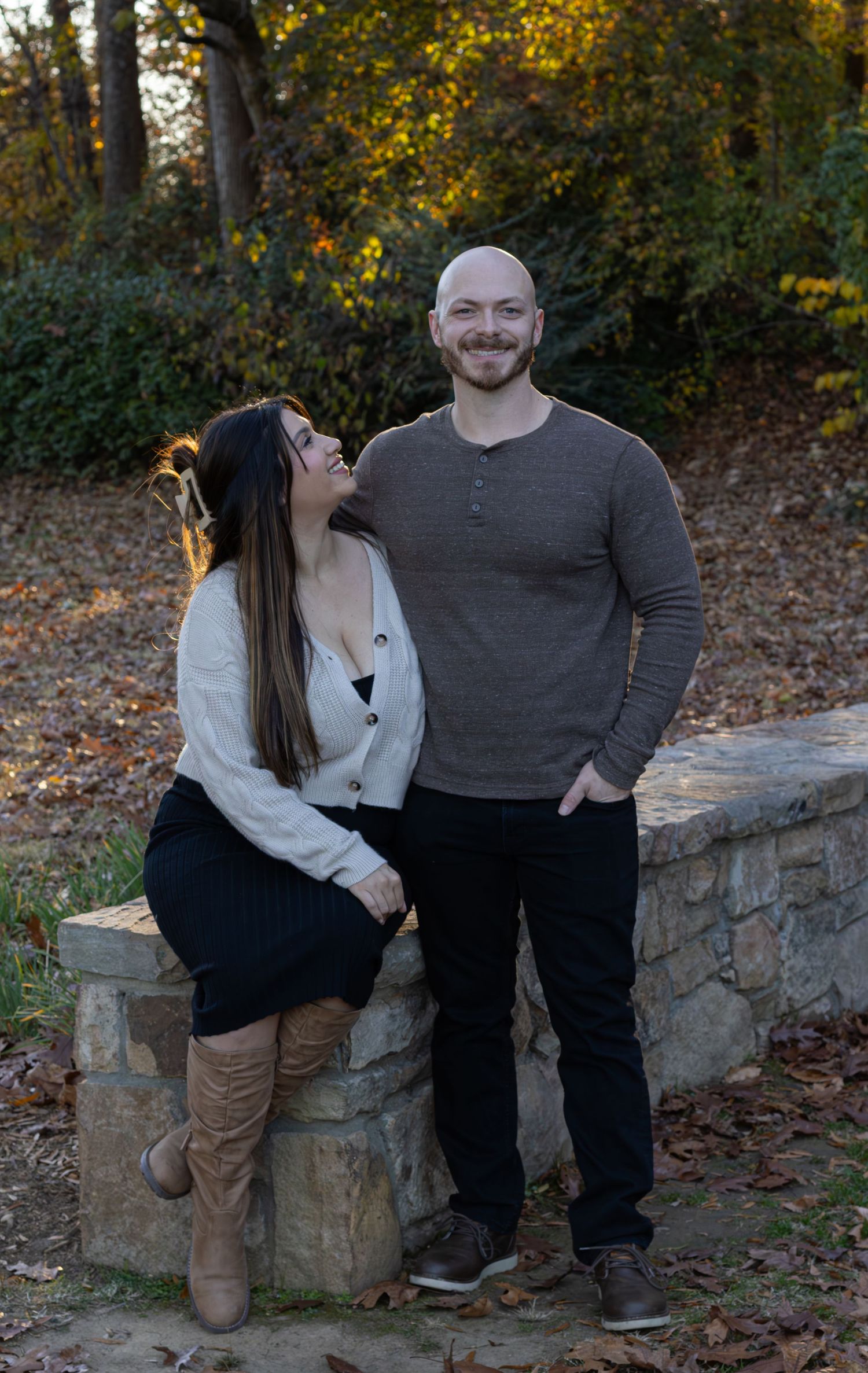 Husband and wife. the wife is sitting looking up at her husband while he's looking at the camera. The lighting is making a halo around them