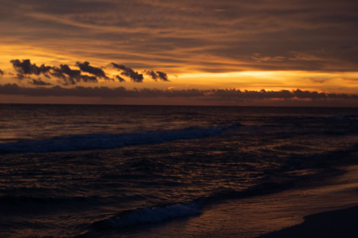 a sunset at its prime time showcasing many different colors. the ocean water is going into soft waves