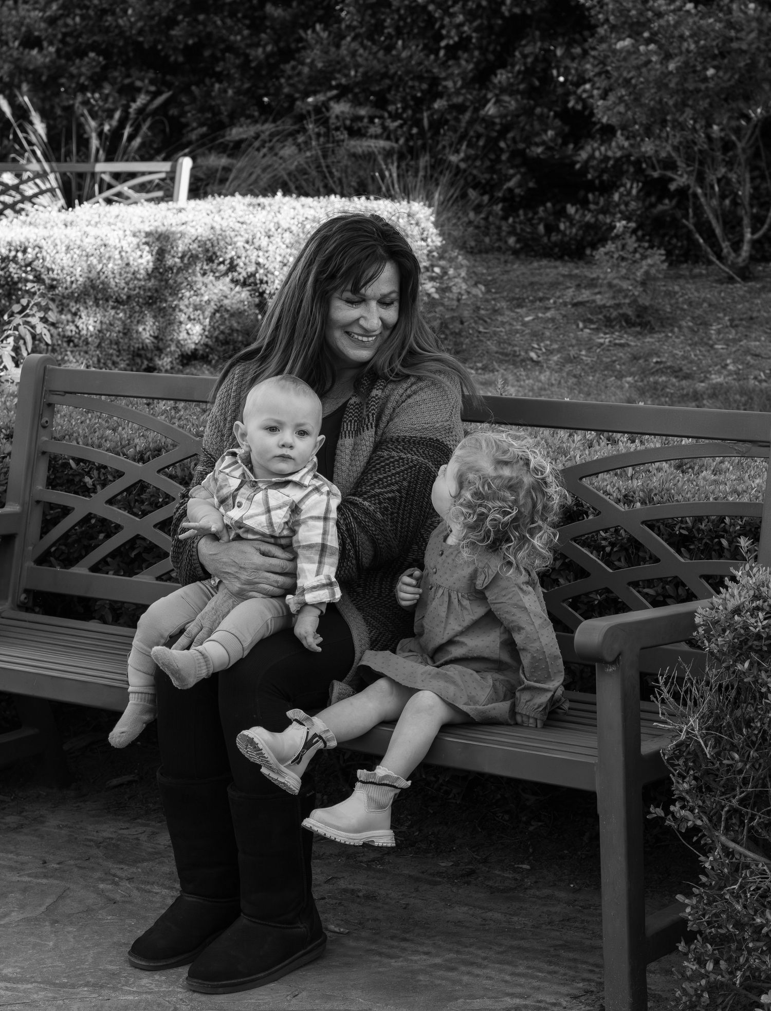 Black and white picture showing a grandma with her two grandkids on a bench in the park.