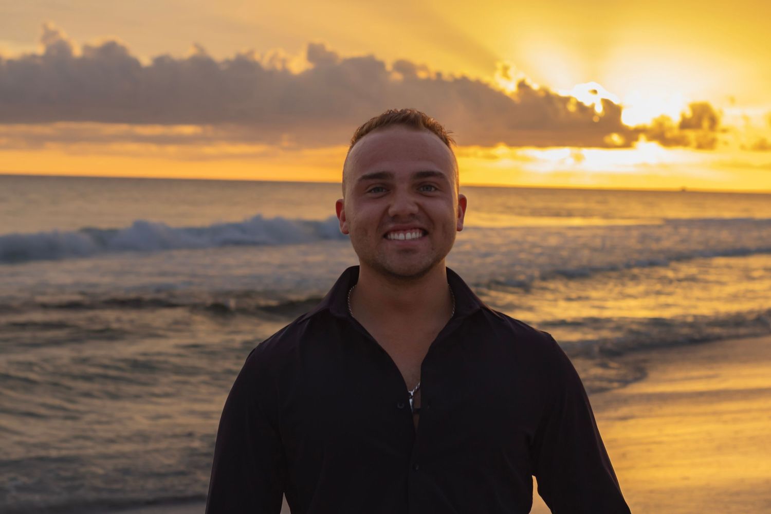 a male up close portrait at the peak sunset time. capturing the sun going down with a hue of orange sky. he is the center of the photo