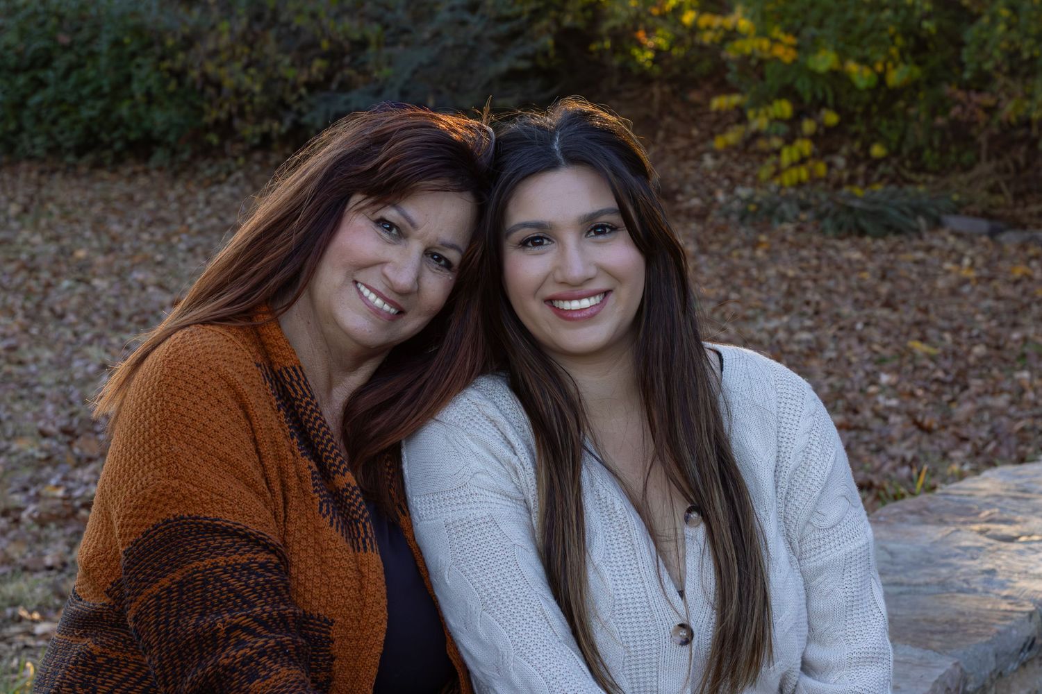 A mother and daughter picture where they're sitting together at the park and the sun is behind them. It a special memory together.