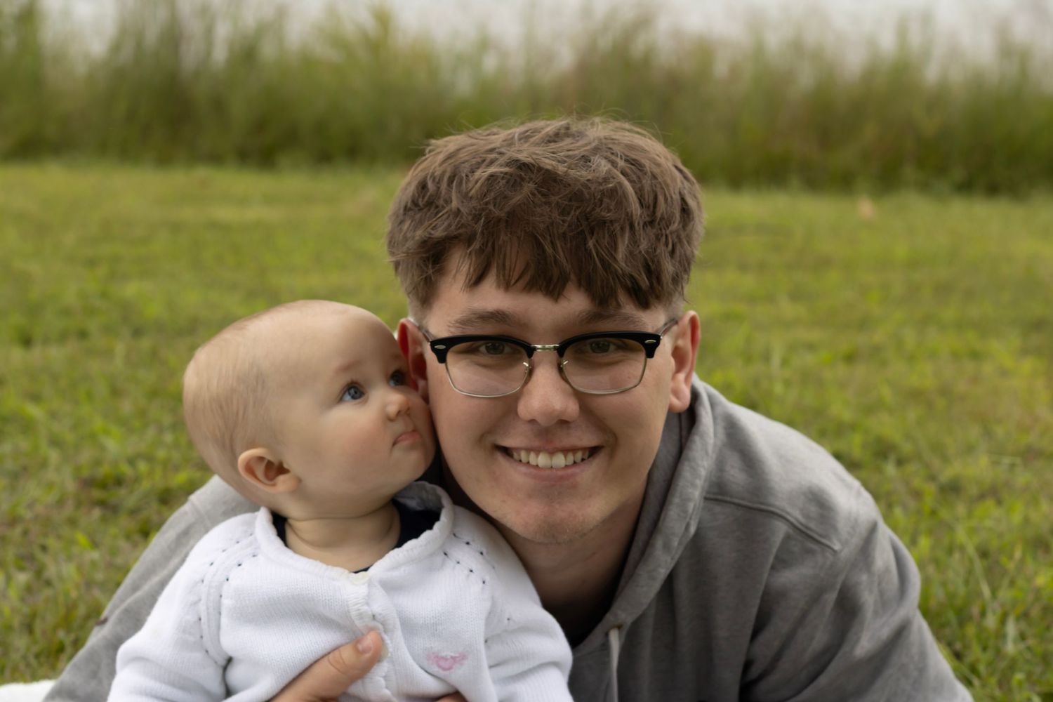 this is a father and daughter picture taken outside. the little girl is looking at her dad and he is looking at the camera