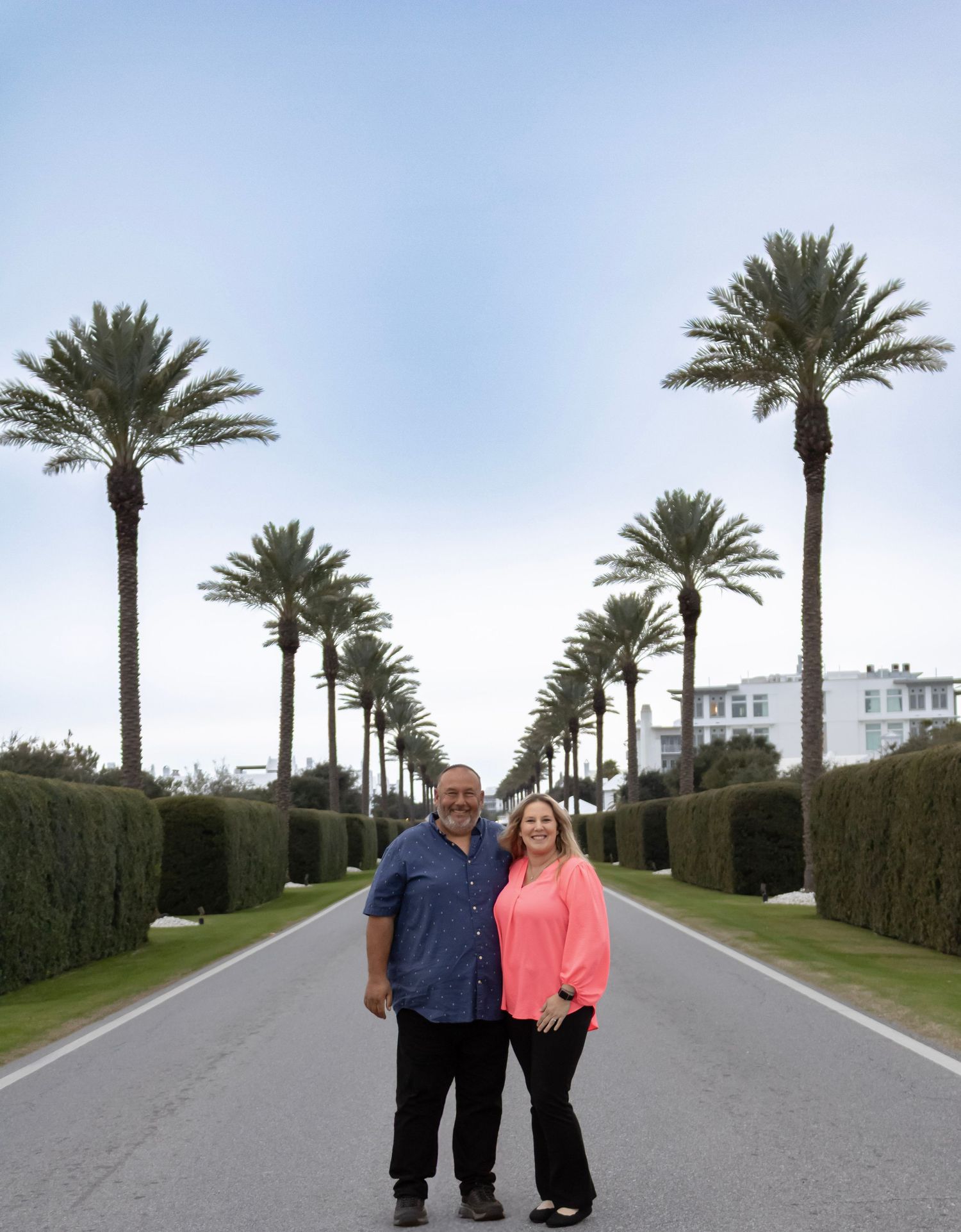 a picture a couple standing in front of a row of palm trees in Panama city, Florida. the sky is blue and the outfits make them pop