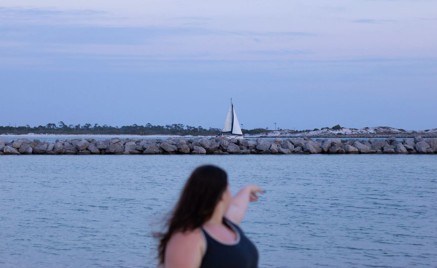 my model is out of focus while a sailboat behind her is. she is pointing to it while it's blue hour.
