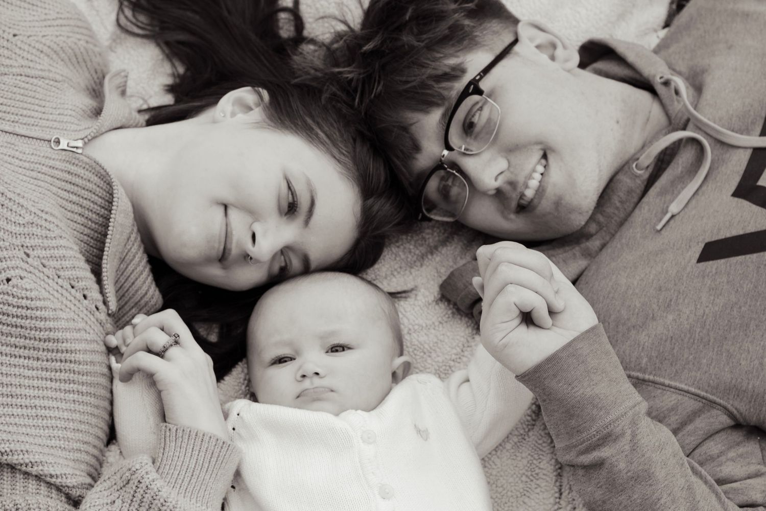 A family picture in black and white. A mother and father are looking at their child with love. They are laying on a blanket
