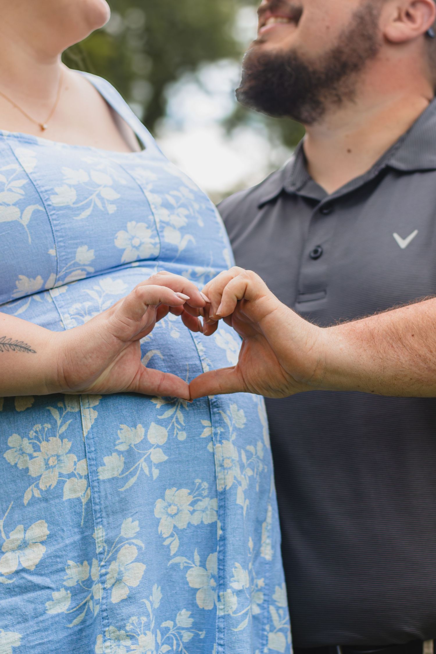 Couple making a heart shape with their hands over pregnant woman's baby bump outdoors.