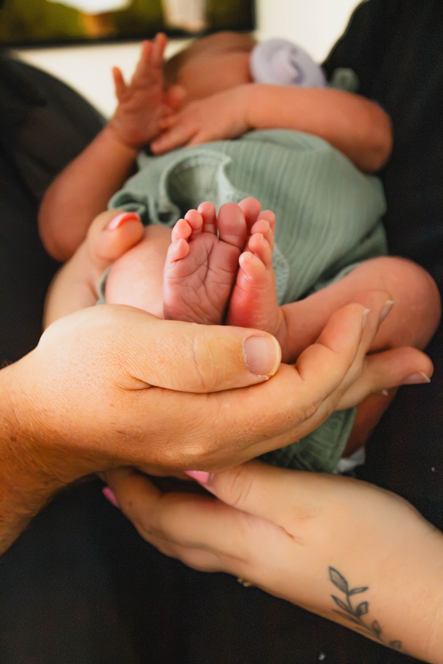 Parents hands cradling tiny newborn baby feet in green outfit close-up.