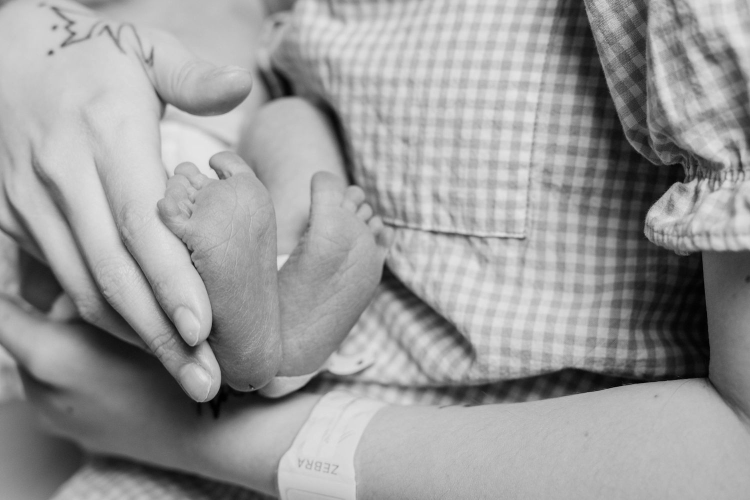Black and white photo of mother holding newborn babys tiny feet in hospital.