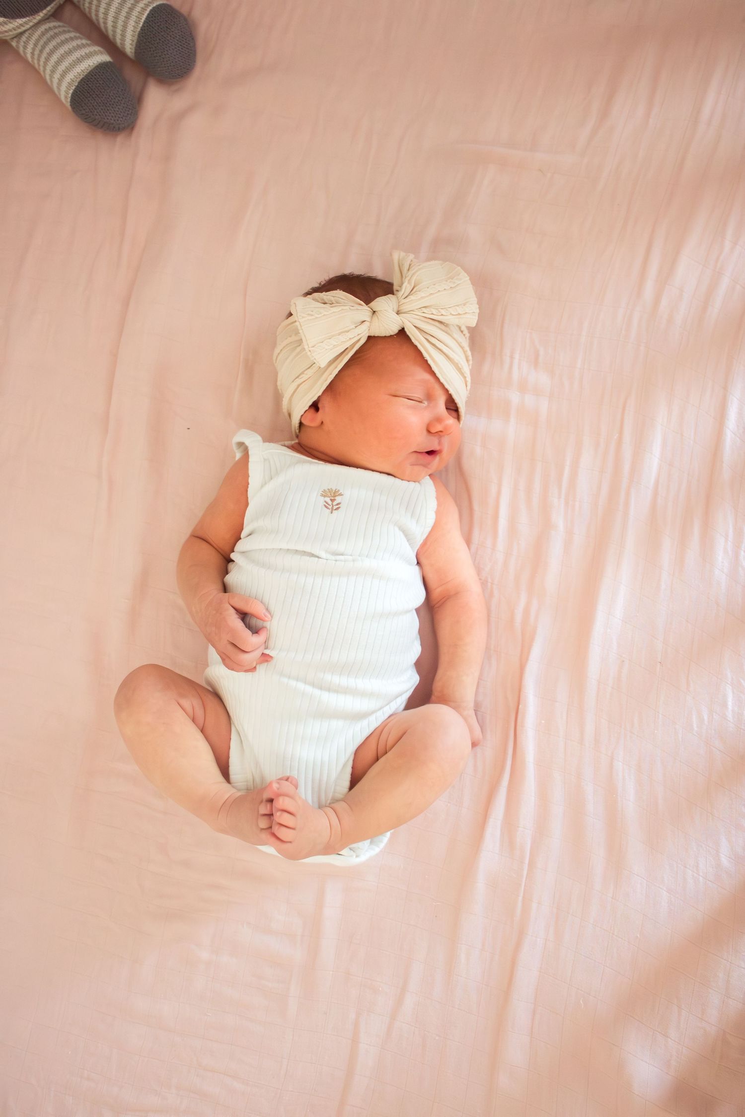 Sleeping newborn baby girl in white romper and bow headband lying on pink blanket.