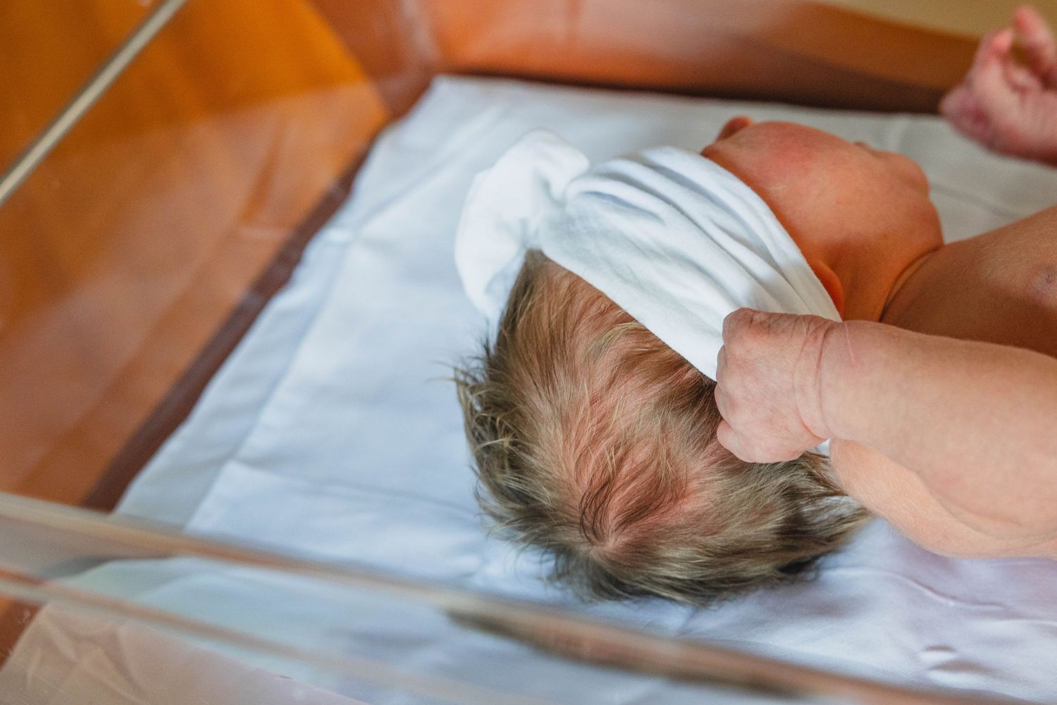 Newborn baby lying on white blanket in hospital bassinet with full head of hair.