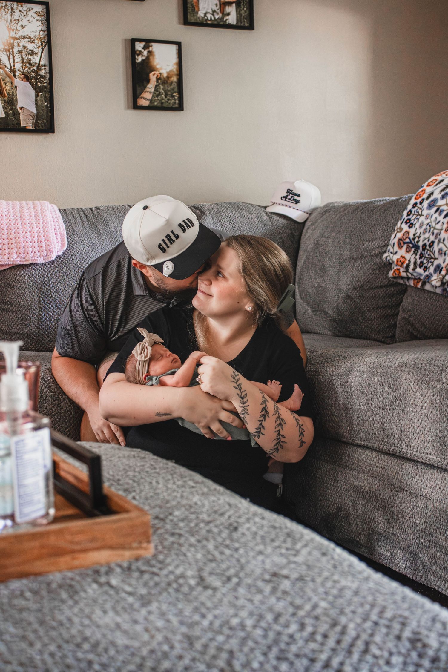 New parents sitting on couch together holding their newborn baby at home.