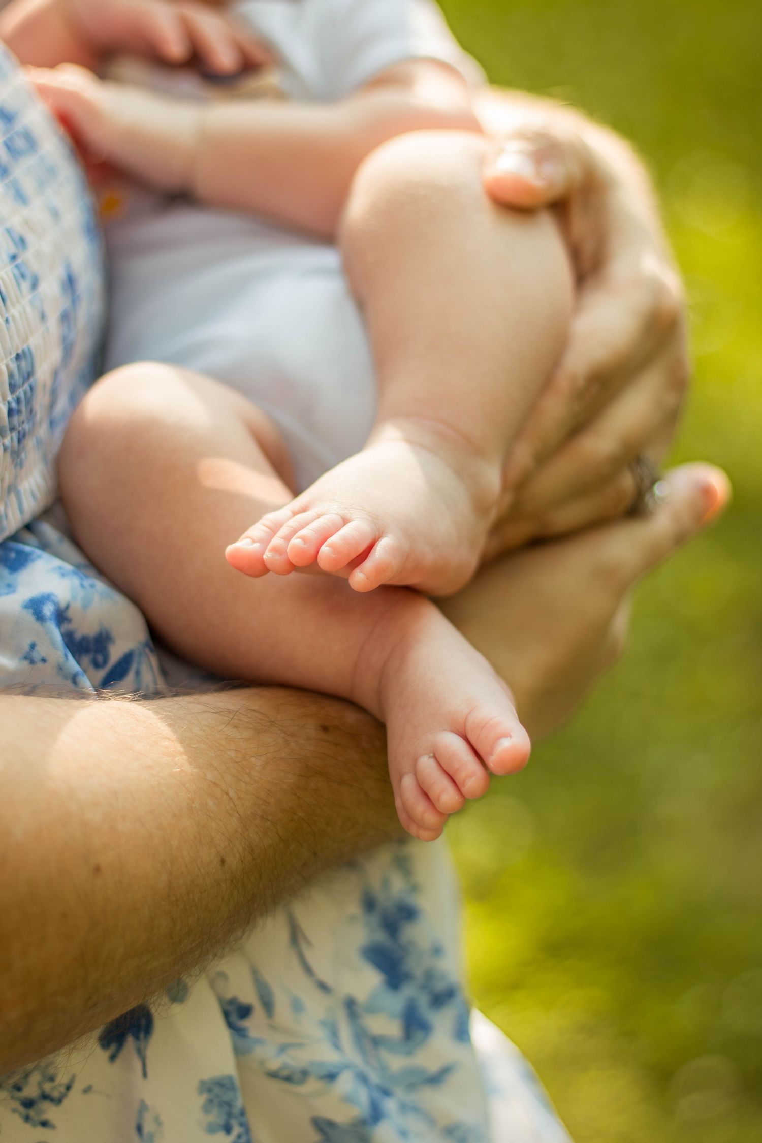 Close-up of newborn baby feet resting in parents arms outdoors in sunny garden.