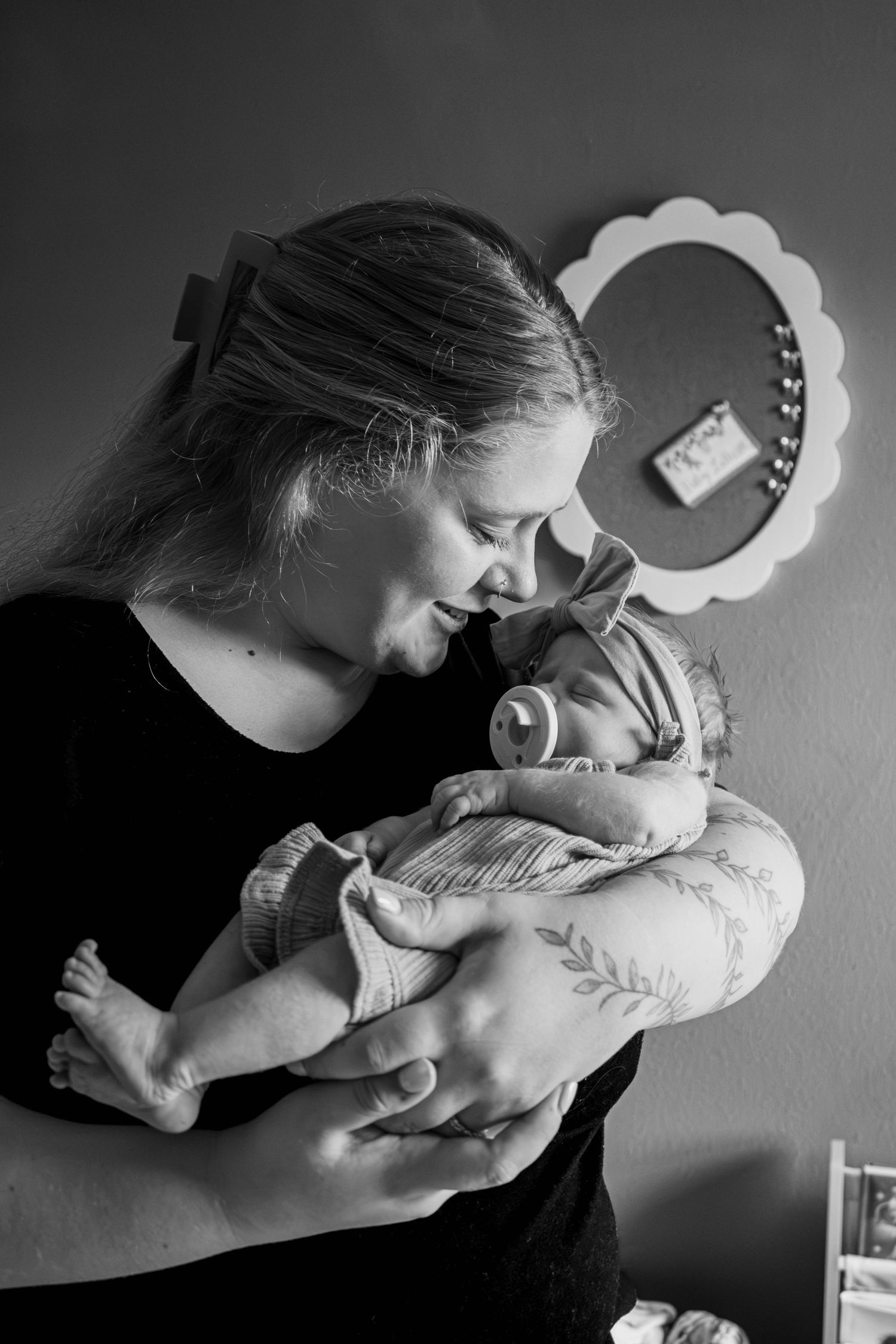 Black and white photo of mother smiling and holding sleeping newborn baby indoors.