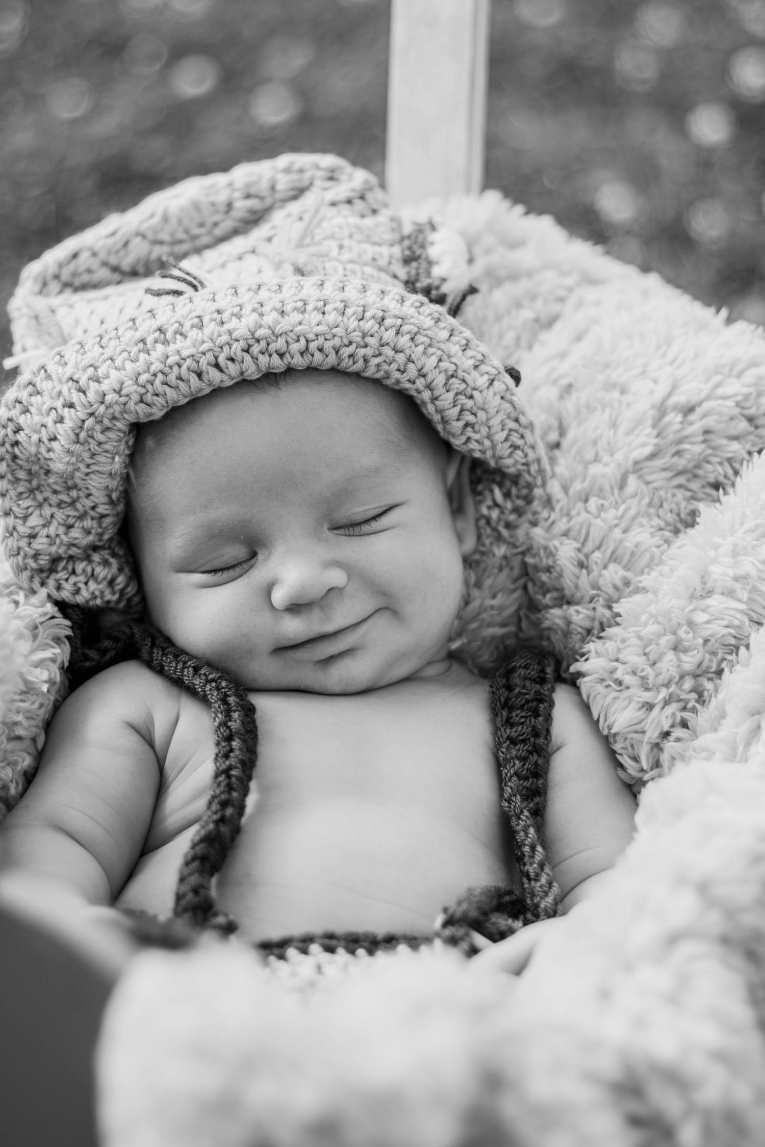Black and white portrait of smiling newborn baby wearing knit hat nestled in soft blanket.