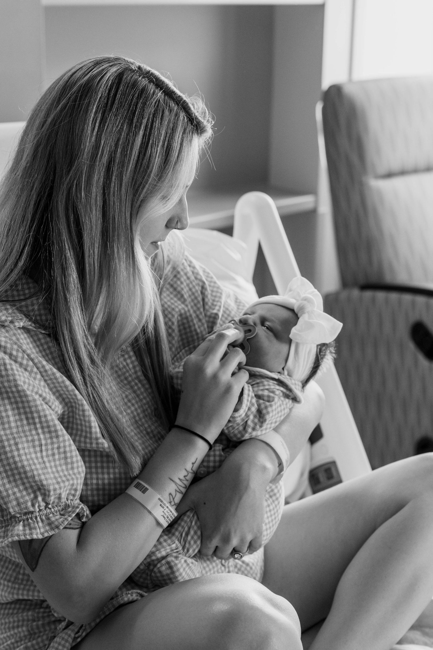 Black and white photo of new mother in hospital gown cradling her newborn baby.