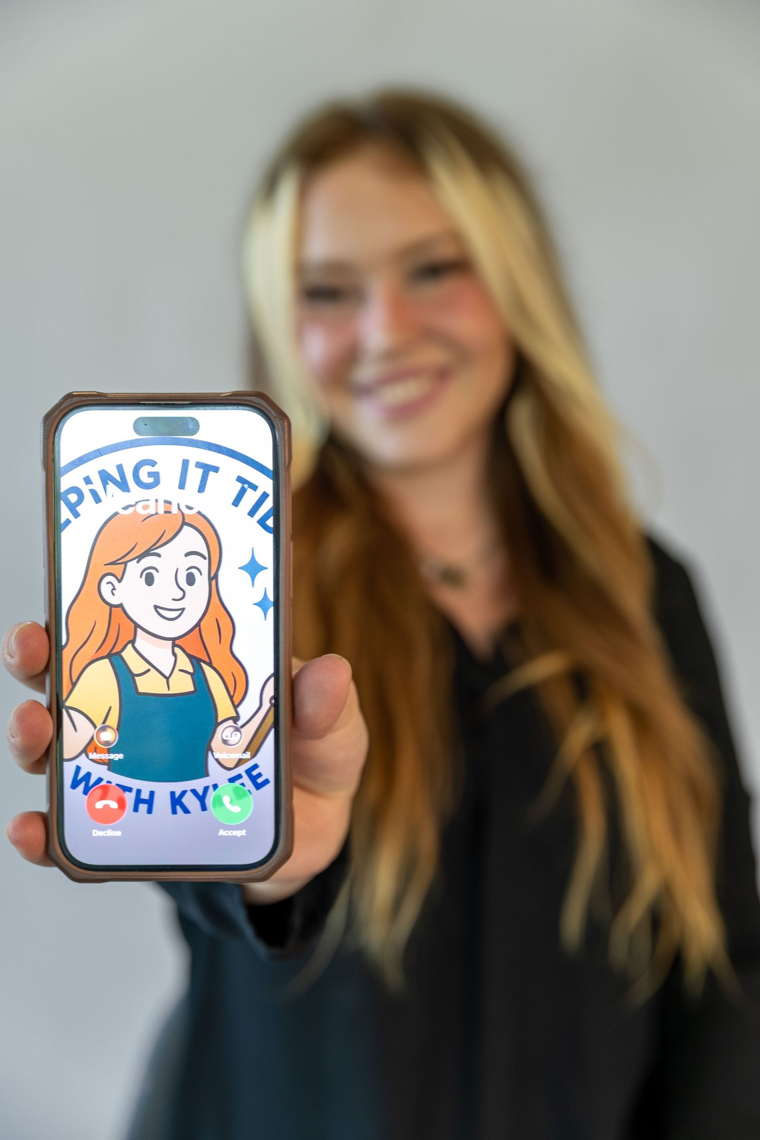 Smiling blonde woman holding phone displaying cartoon logo reading 'Keeping It Tidy with Kylee'. Branding session Acworth, GA