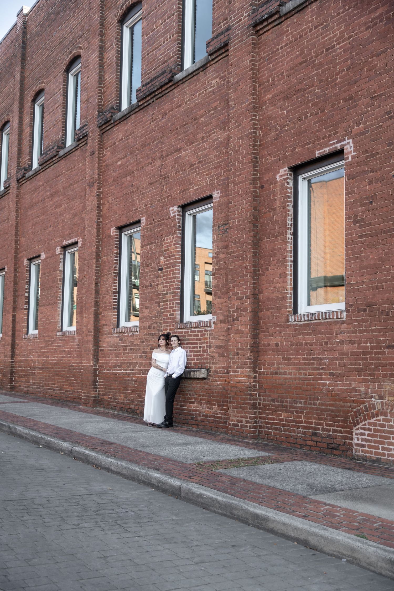 Couple in wedding attire posing against a red brick building on a cobblestone street. Downtown Rome, GA Jessica M Cooper Photography LLC