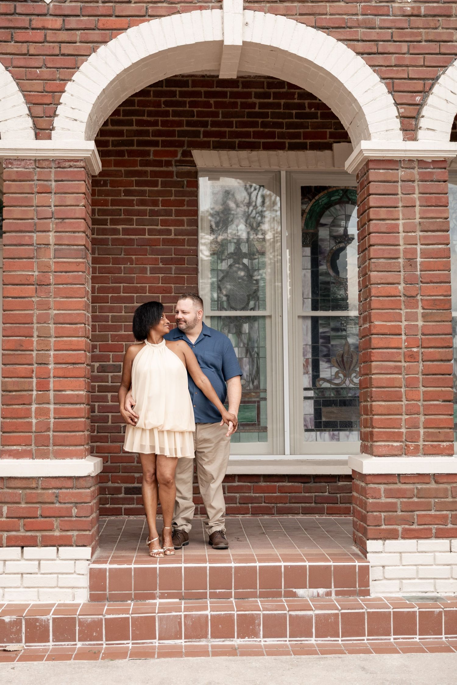 Couple embracing and smiling at each other on brick building steps with arched windows backdrop. Rockmart, GA