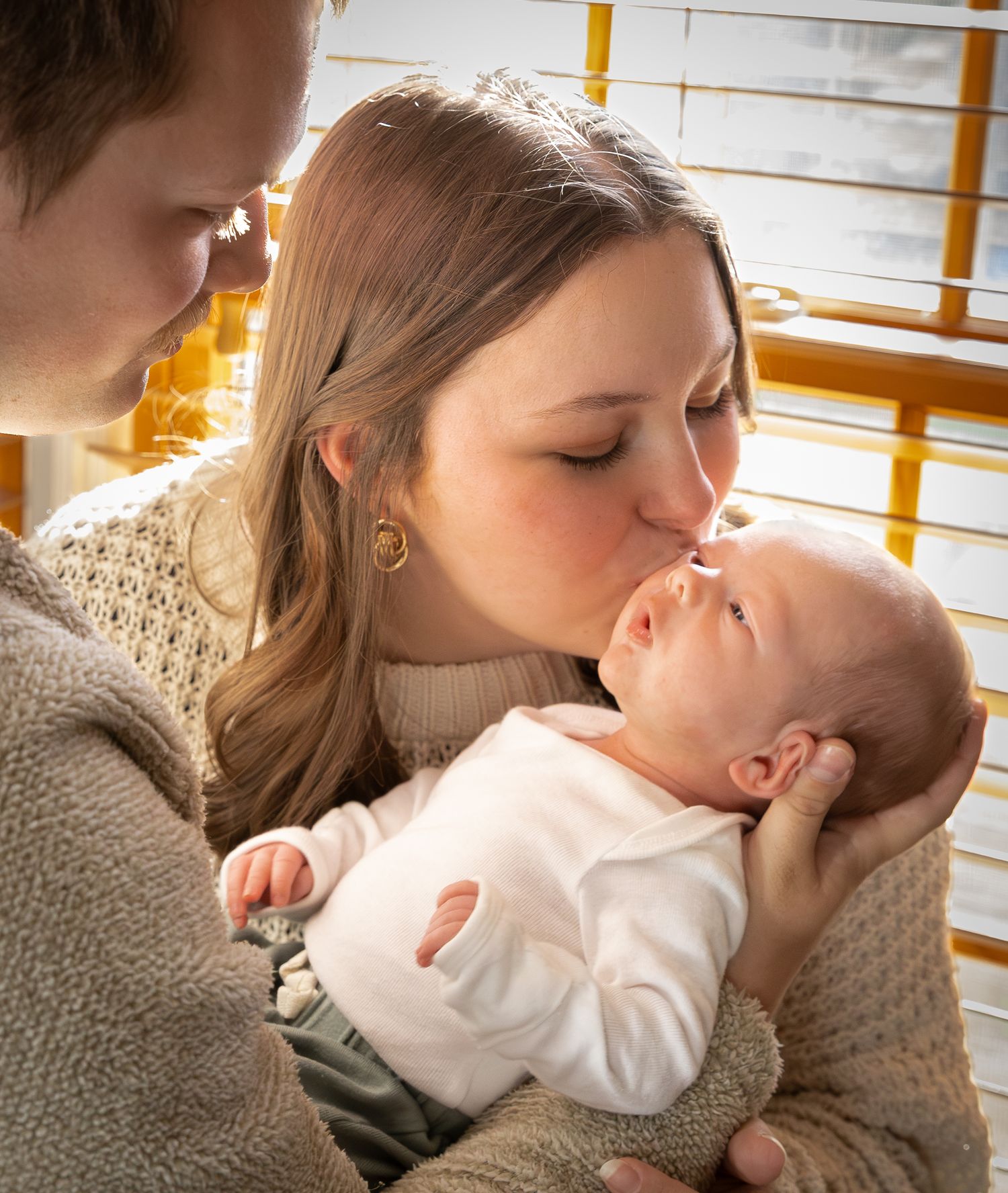 A tender moment captured as a mother in a cream sweater kisses her infant baby.  Rome, GA Jessica M Cooper Photography LLC
