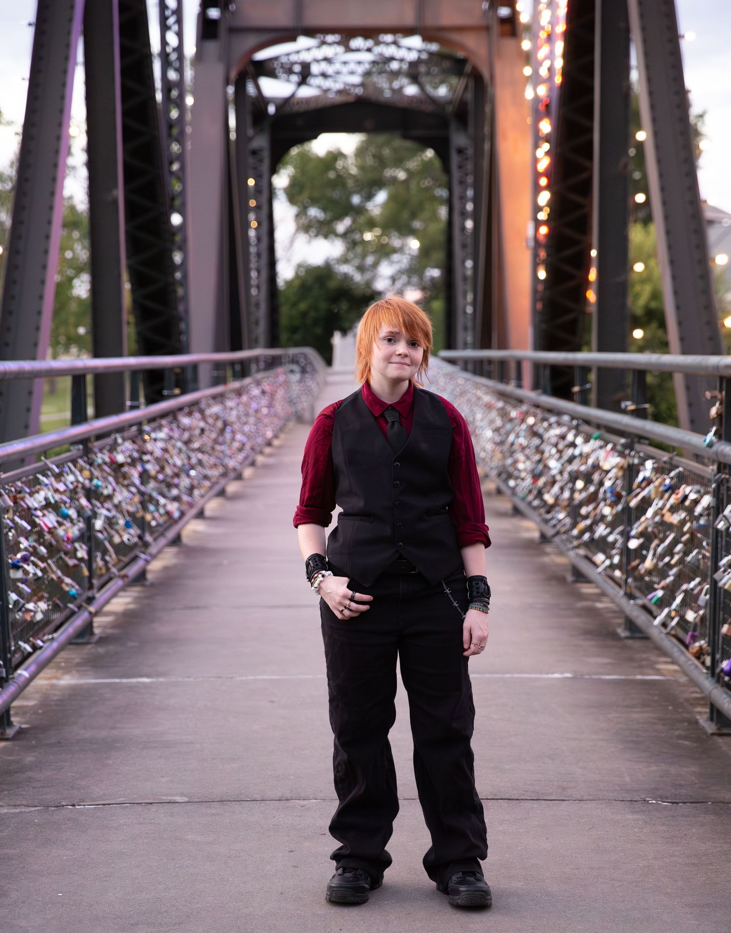 Person with orange hair in black vest and red shirt standing on a lock bridge with metal trusses. Downtown Rome, GA