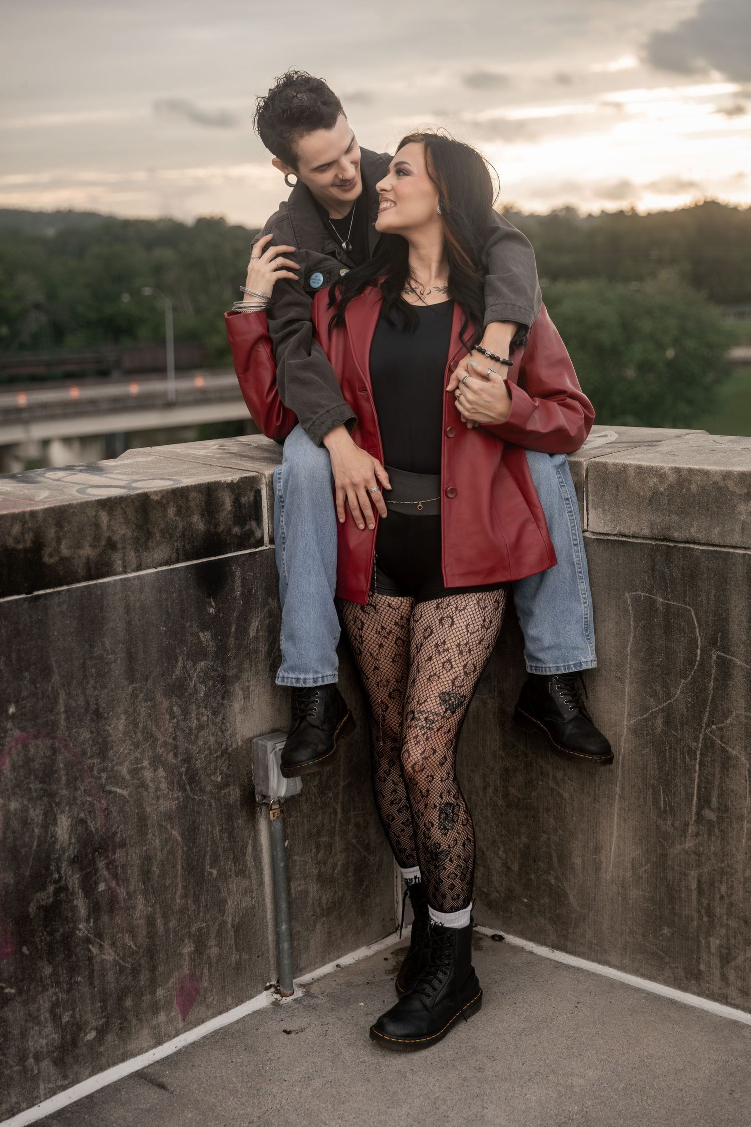 A couple shares a romantic moment on a rooftop at sunset, woman in red jacket and patterned tights, man seated on ledge.Downtown Rome, GA
