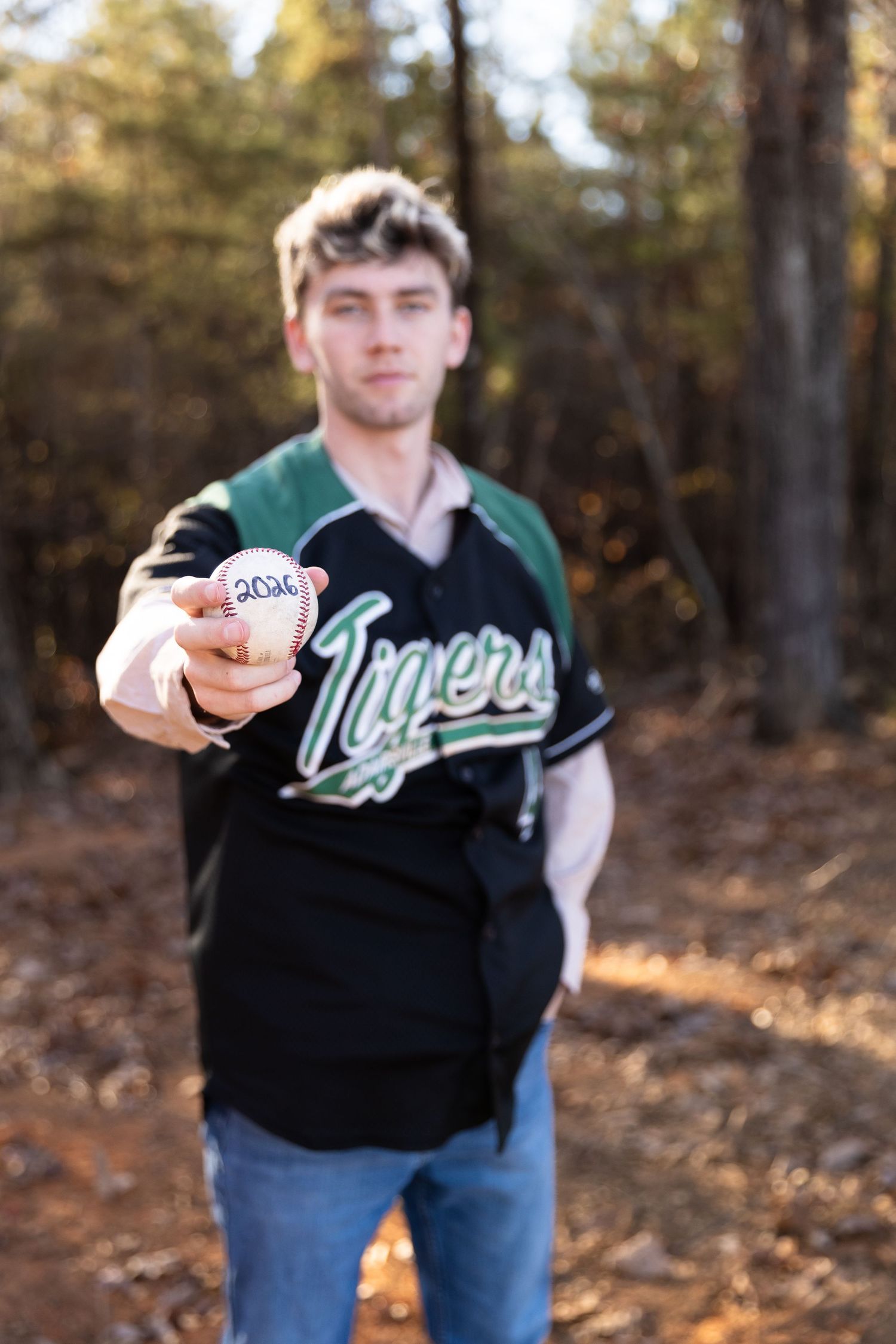 Senior male in athletic wear holds a baseball while posing in a wooded area- Northwest Georgia Jessica M Cooper Photography LLC