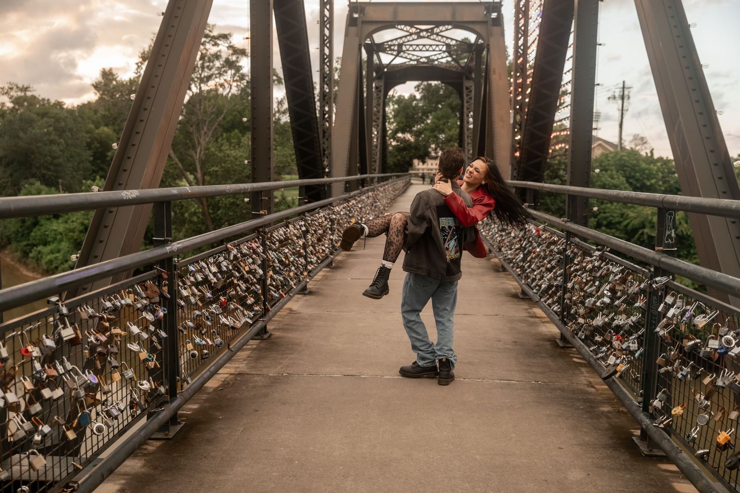 A couple walks on a bridge adorned with love locks, one person carrying another on their back at sunset. Downtown Rome, GA