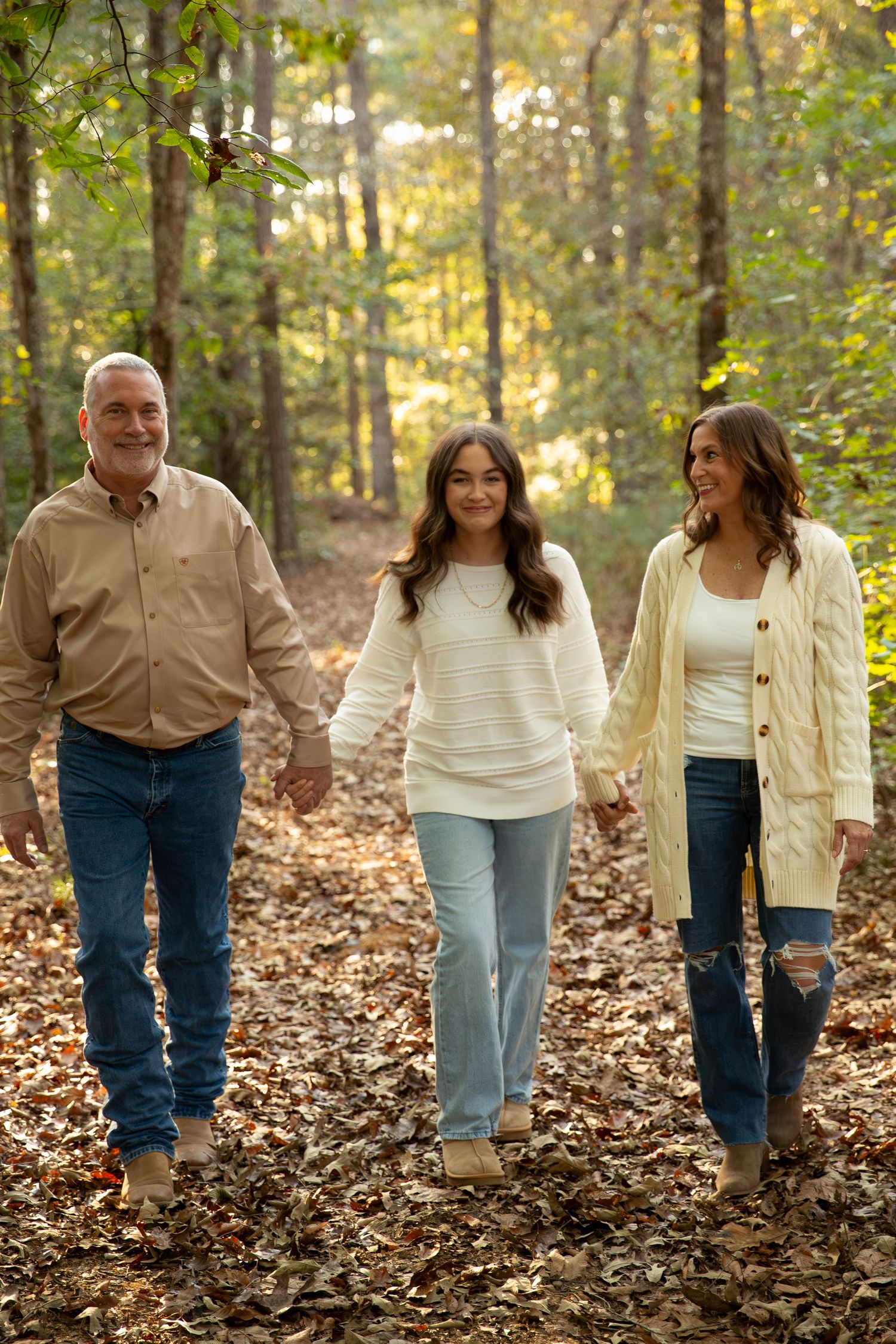 Family group walking together through fallen leaves in coordinated neutral outfits in Northwest GA by Jessica M Cooper Photography LLC