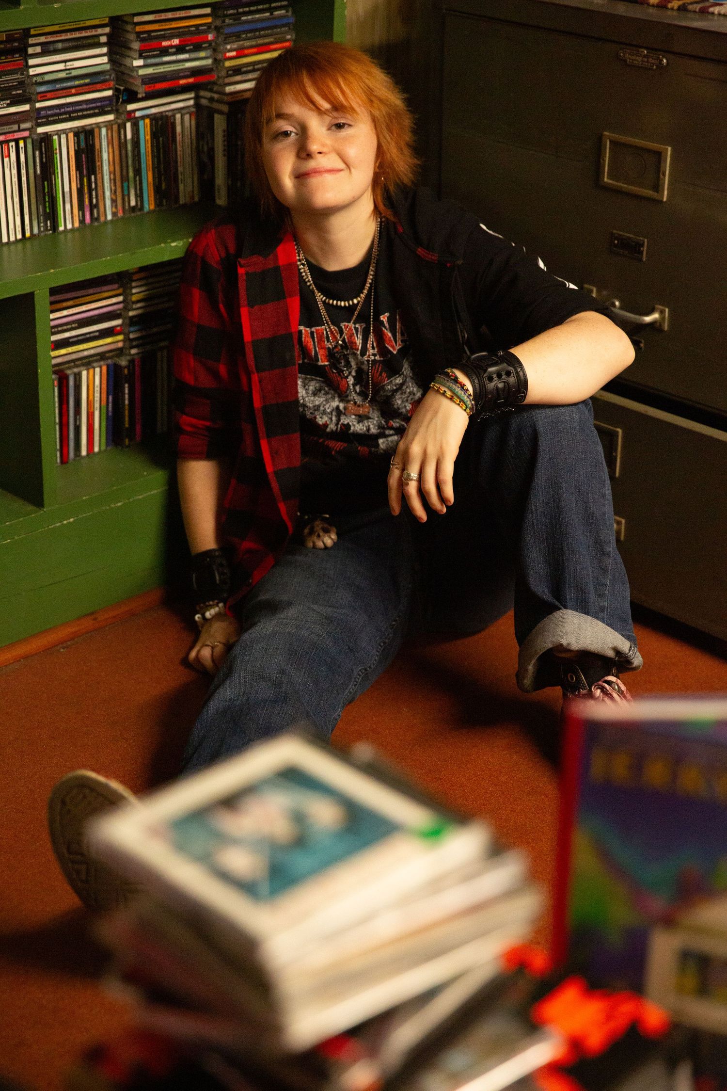 A young person with red hair sits on the floor smiling, wearing a plaid shirt, jeans Downtown Rome, GA Jessica M Cooper Photography LLC