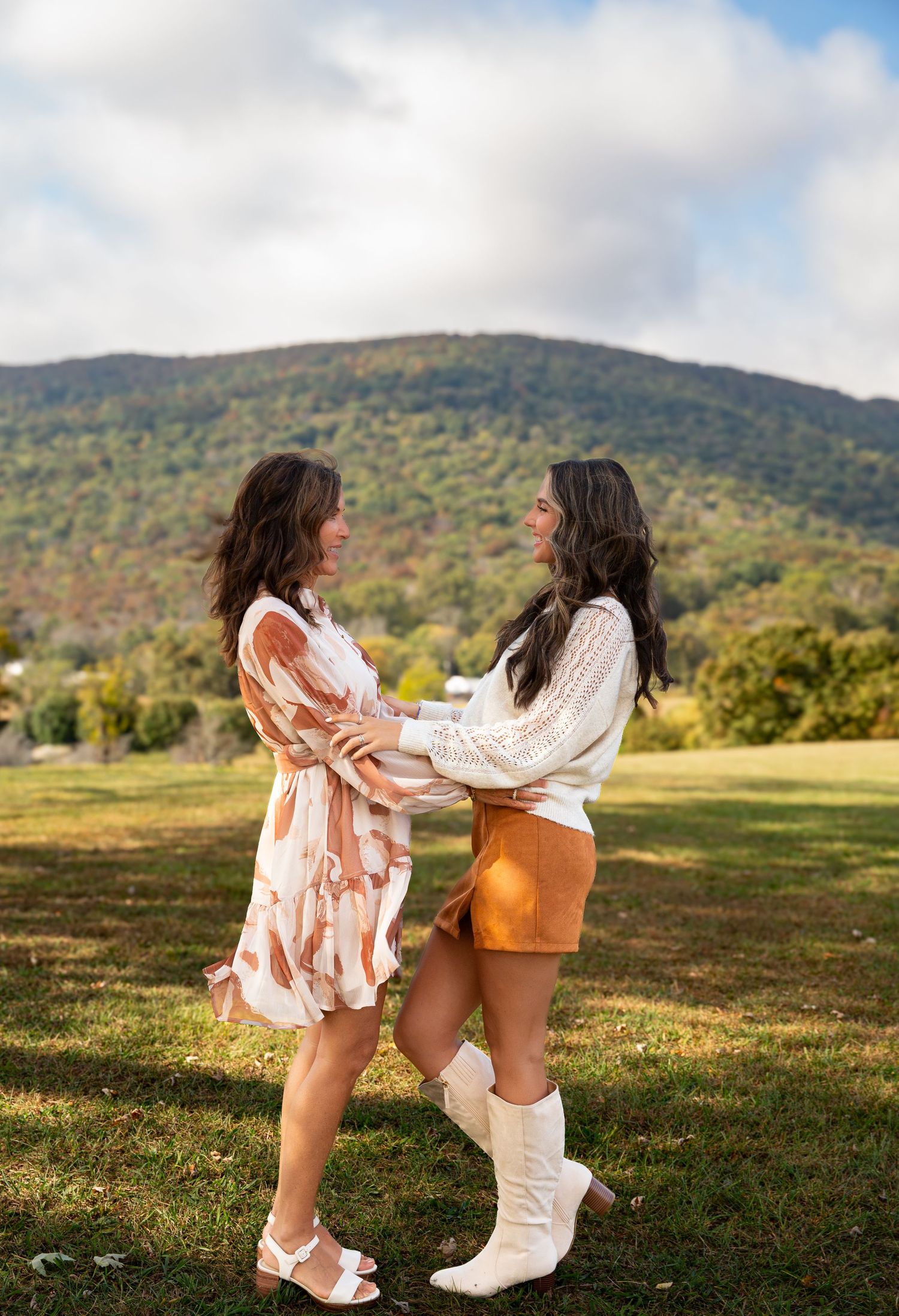 Two people in white dresses dance and twirl together in a grassy field with mountains in the background- Northwest Georgia
