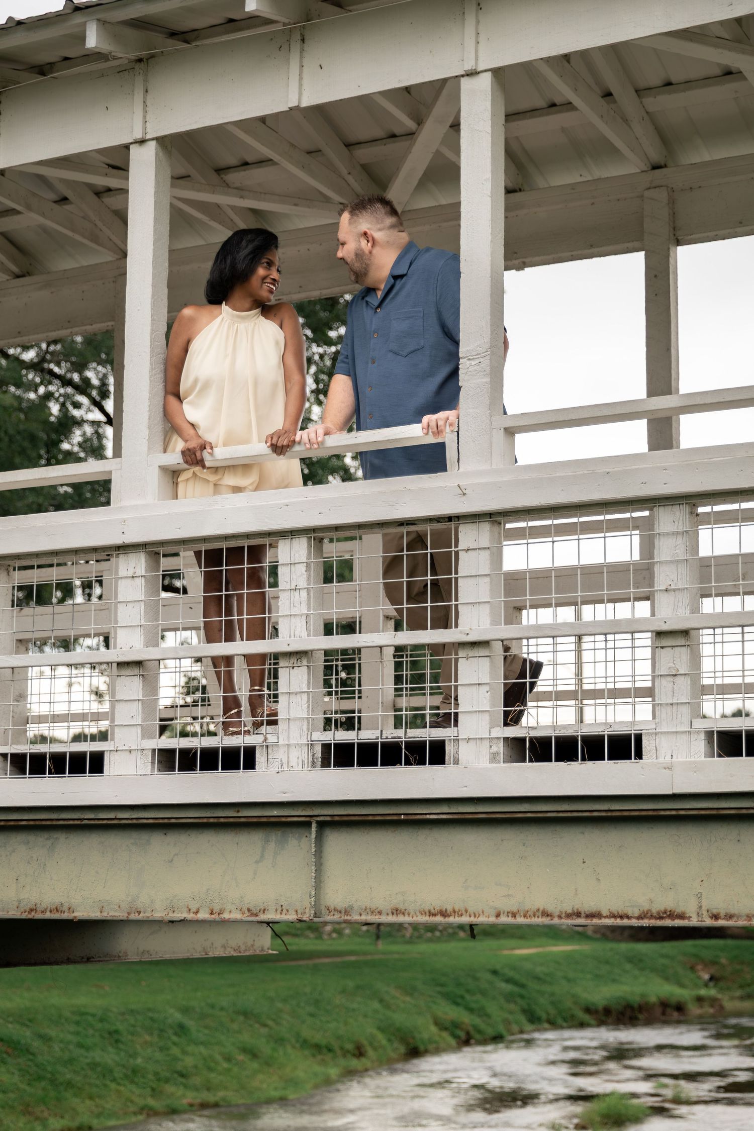 Interracial couple sharing a romantic moment on a white wooden bridge overlooking a green waterway. Rockmart, GA