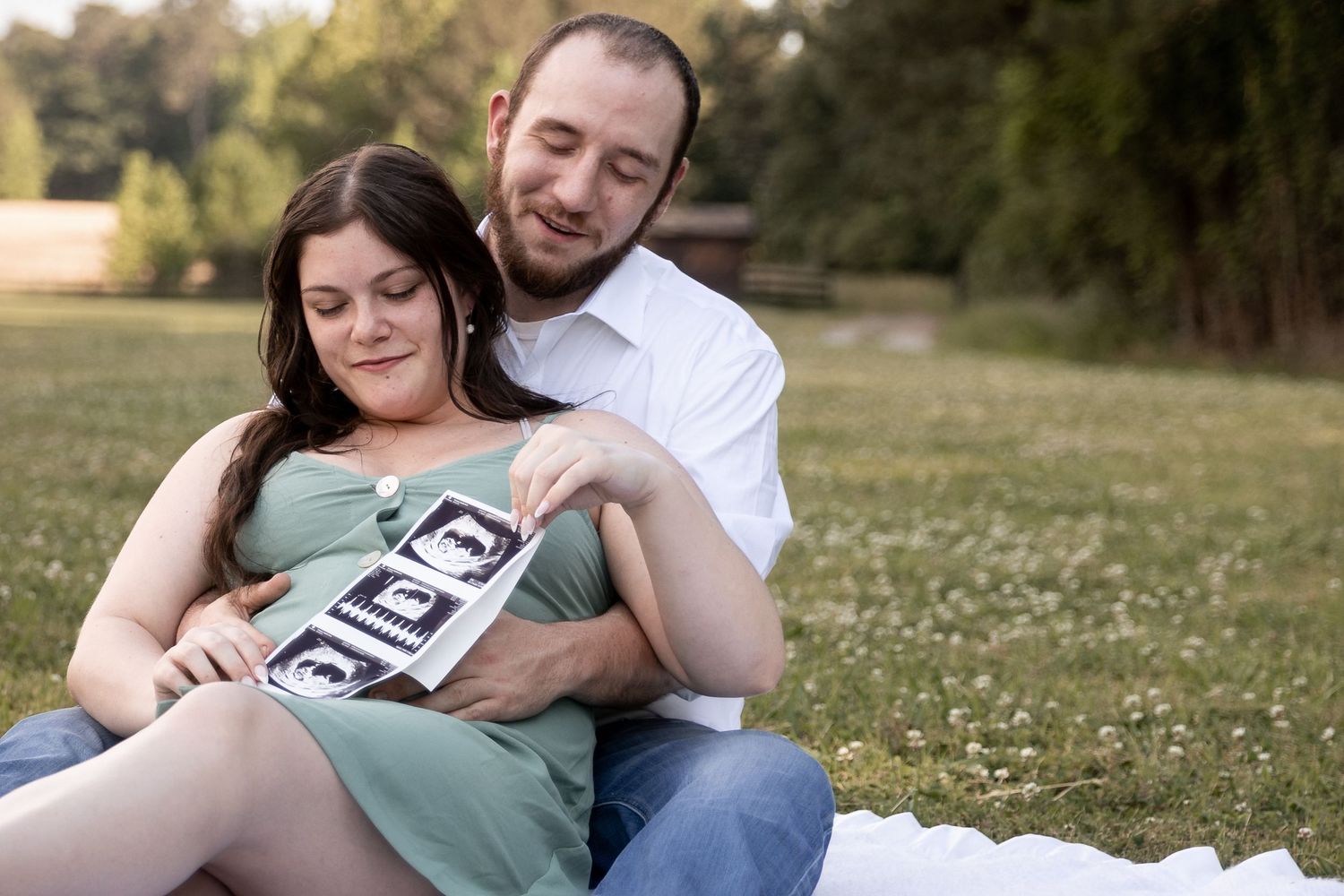 Couple sitting on grass sharing ultrasound photos during outdoor maternity photo session. Frost Chapel Berry College, GA