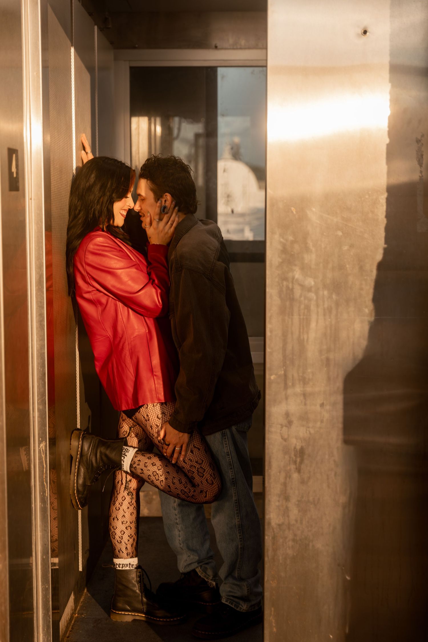 Couple sharing a passionate kiss in a dimly lit elevator, woman in red jacket and fishnet tights. Downtown Rome, GA