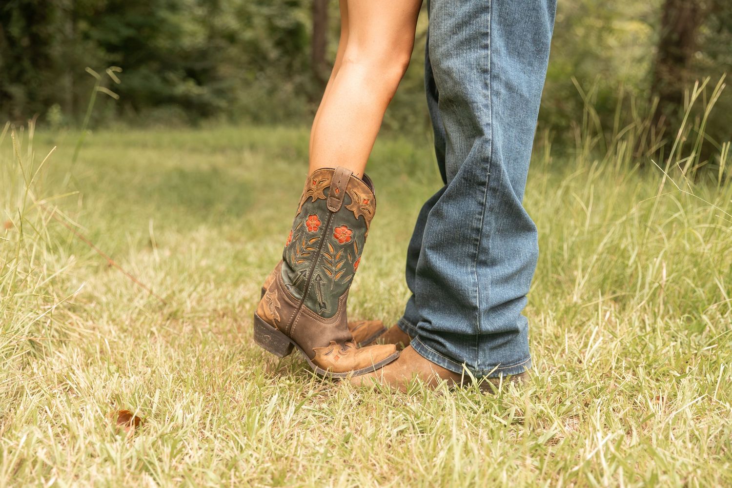 Close-up of cowboy boots and jeans standing in a grassy field, showcasing Western country style footwear. Rome, GA