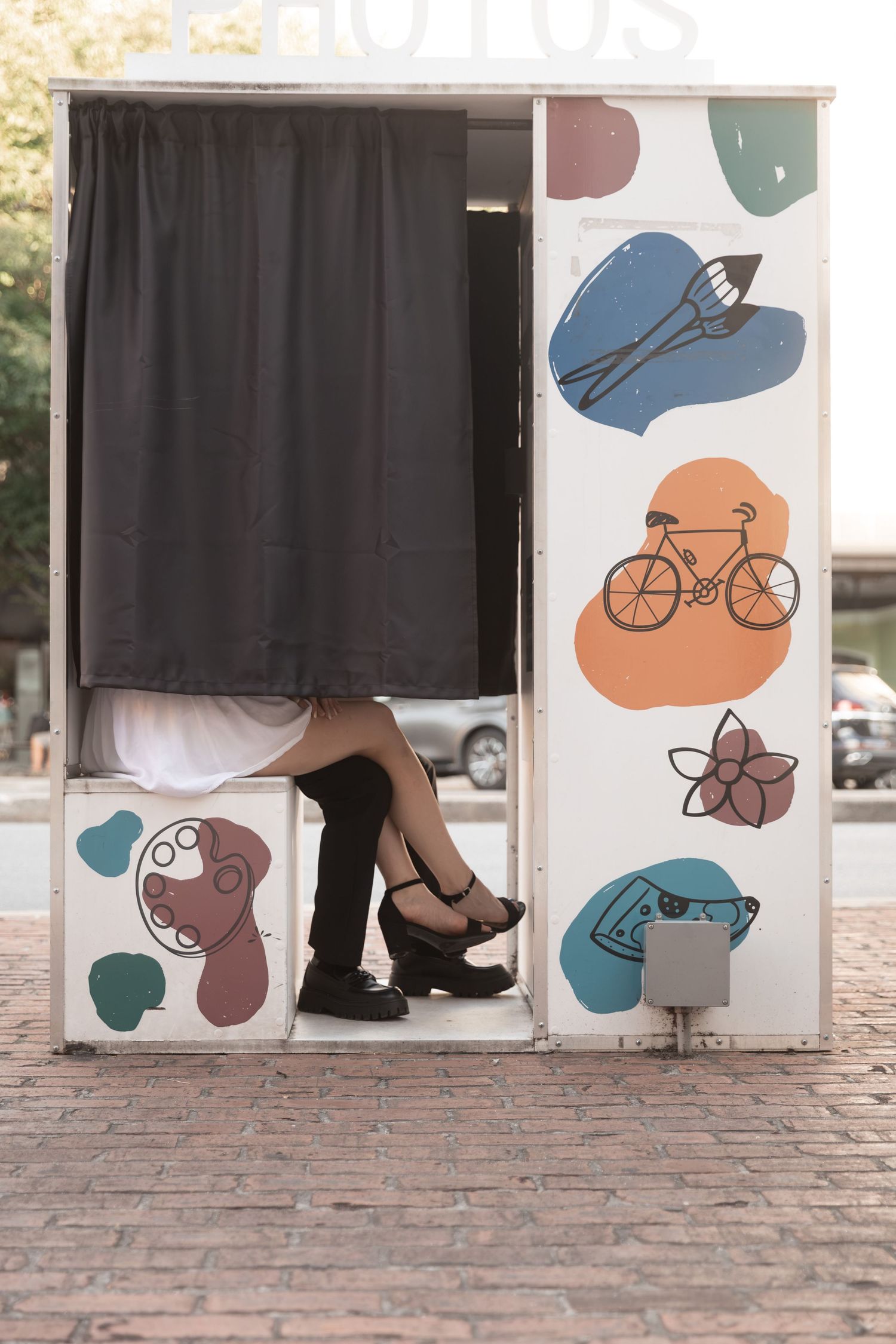 Couple sharing a romantic moment inside a vintage photo booth with colorful illustrated decorations on the exterior. Downtown Rome, GA