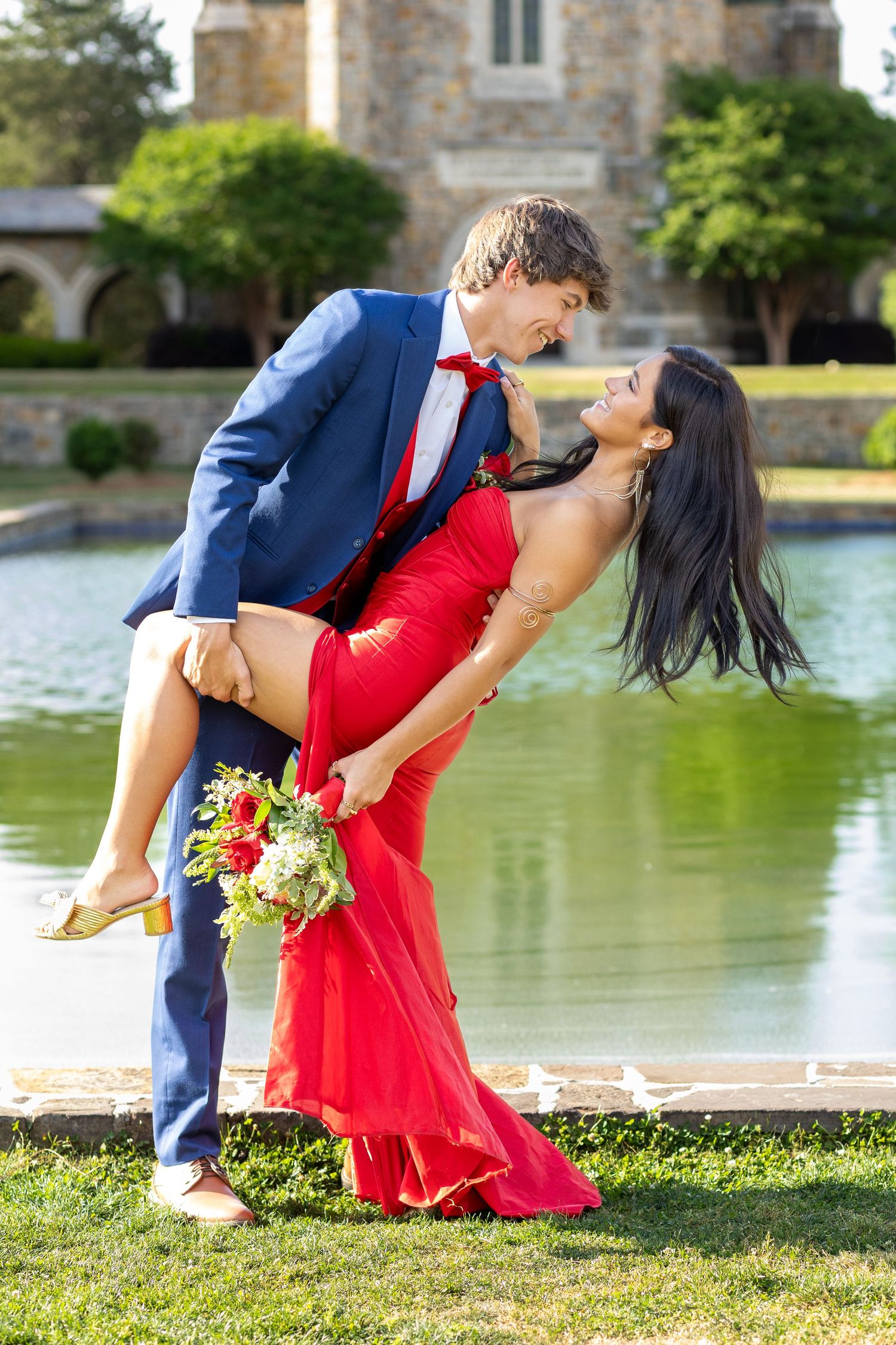 Couple in formal wear dancing by the reflection pool at Berry College. Man in blue suit dips woman in red gown holding bouquet in Rome, GA