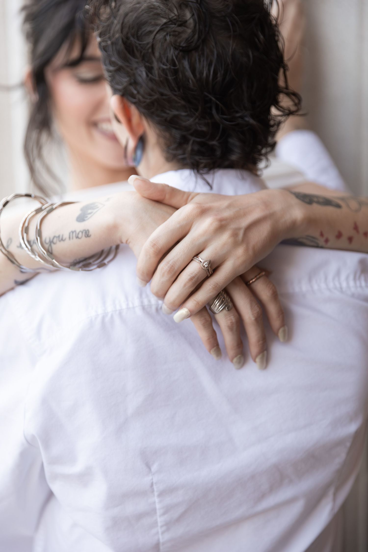 A smiling woman with tattoos and rings embraces a partner in a white shirt, showcasing an engagement ring.  Downtown Rome, GA