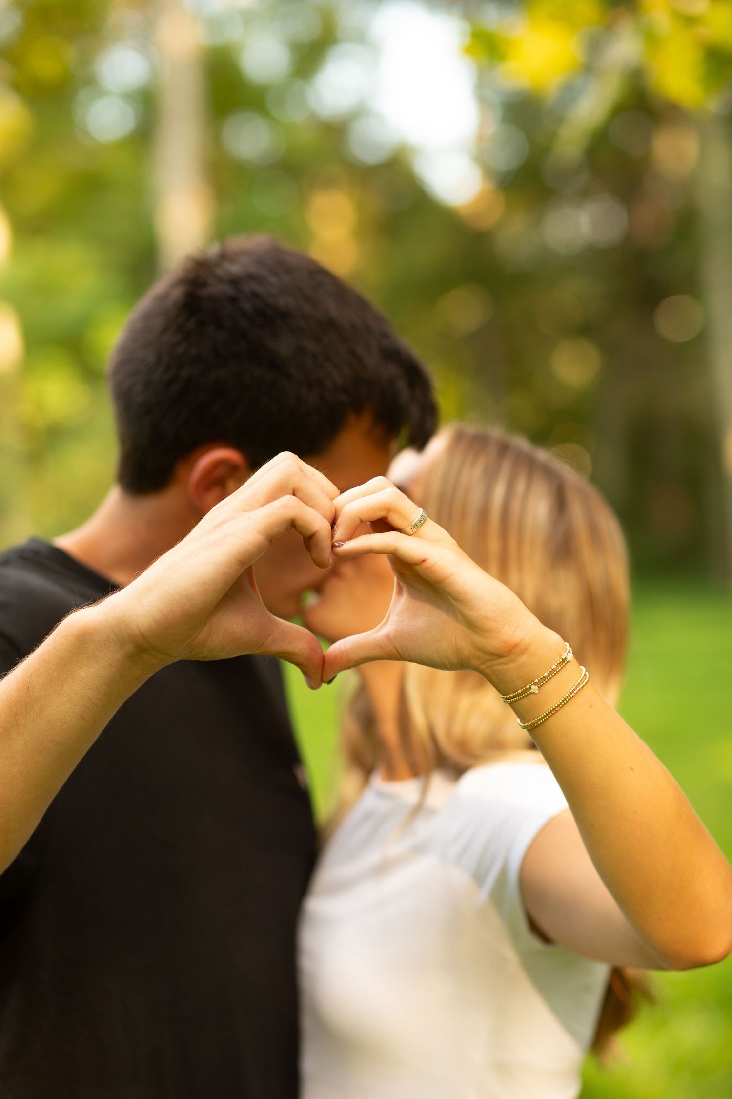 A couple forms a heart shape with their hands against a blurred green outdoor background.  Rome, GA Jessica M Cooper Photography LLC