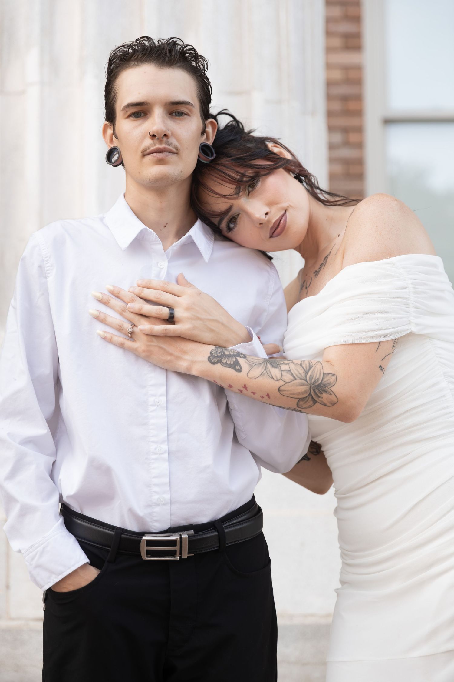Tattooed bride in white dress leans on groom in white shirt and black pants, posing together outdoors.  Downtown Rome, GA
