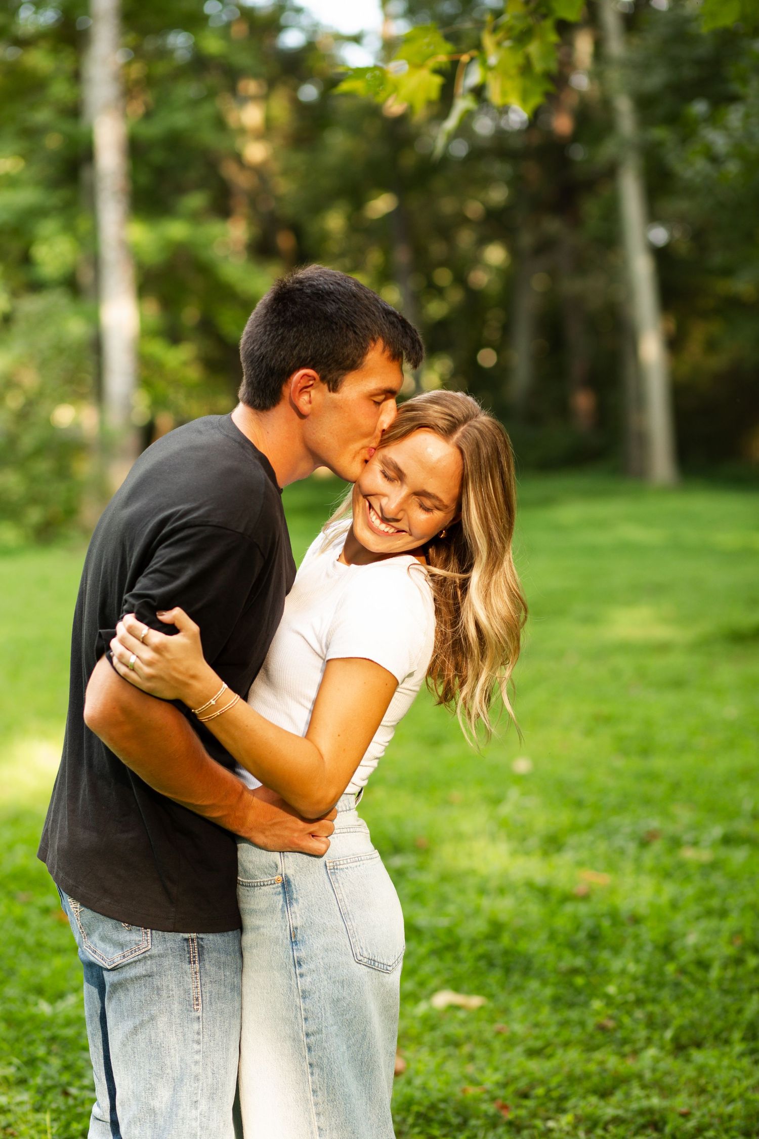 A romantic couple embraces and laughs together on a sunny day in a lush green park setting.  Rome, GA Jessica M Cooper Photography LLC