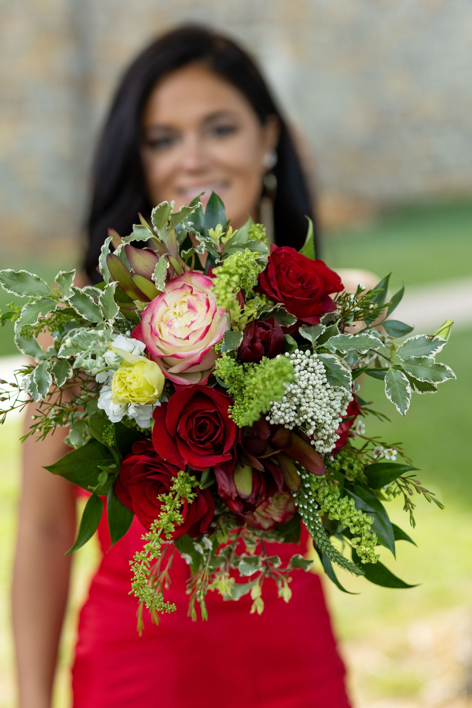 Woman in red dress holding a vibrant bouquet of red roses, pink peonies, and greenery outdoors. Jessica M Cooper Photography LLC Senior Prom