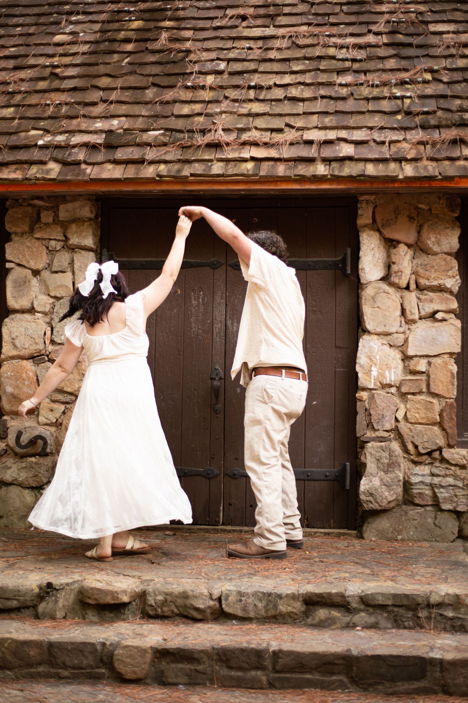 Playful couple dancing and posing against a rustic stone wall with wooden doors at Berry College-Jessica M Cooper Photography LLC Rome GA