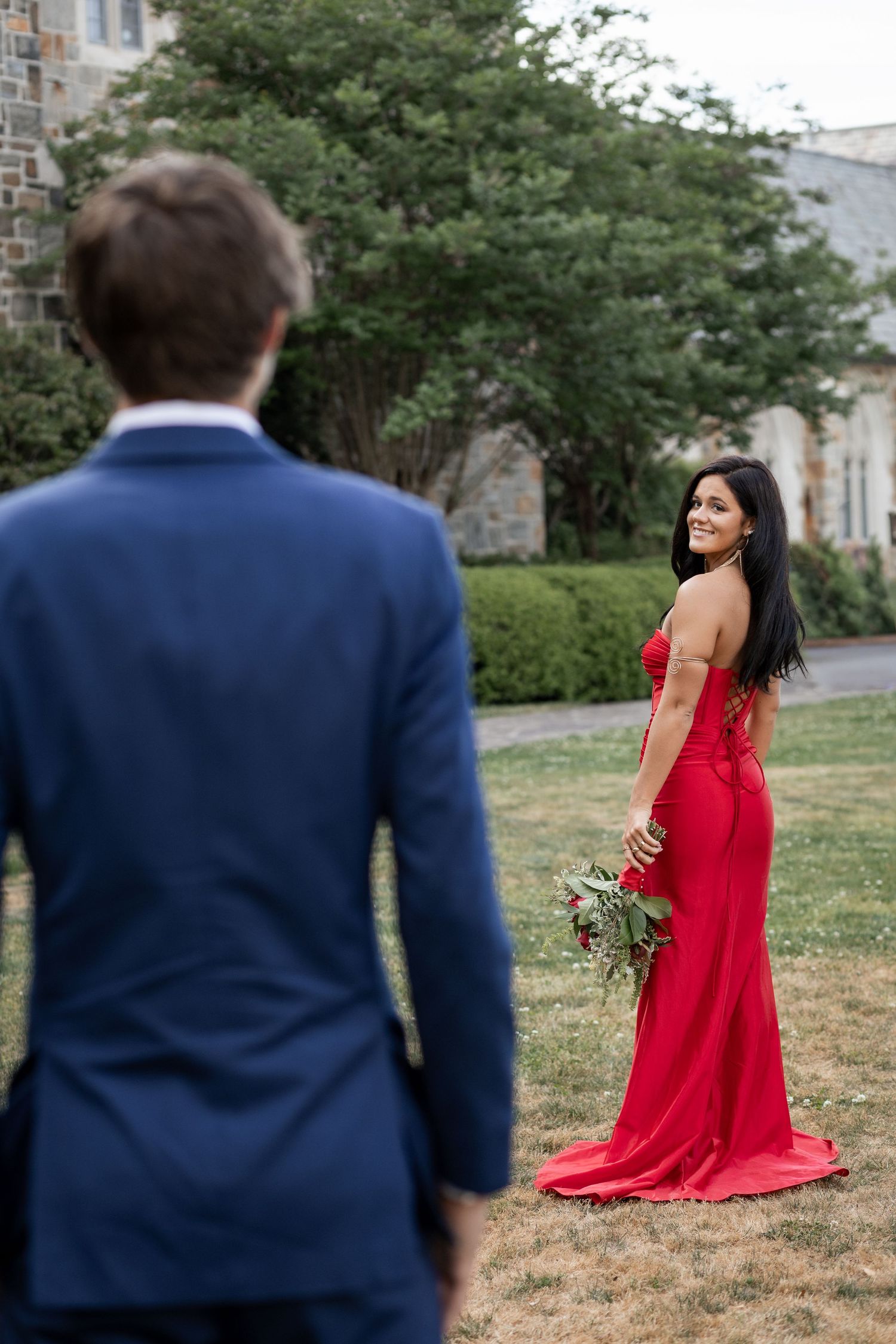 Woman in red gown holds bouquet while smiling at man in navy suit outdoors near Ford building Berry College, Rome ,GA
