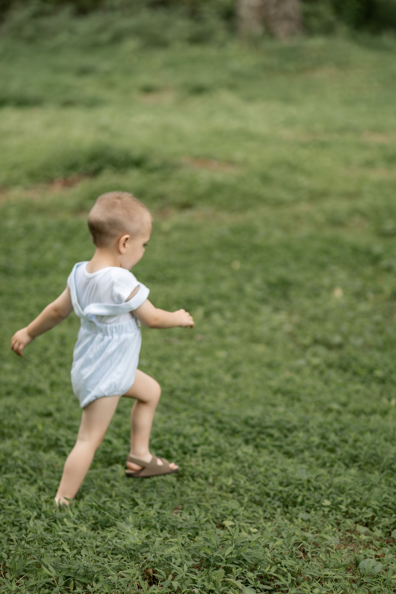Toddler in white romper running on lush green grass outdoors.