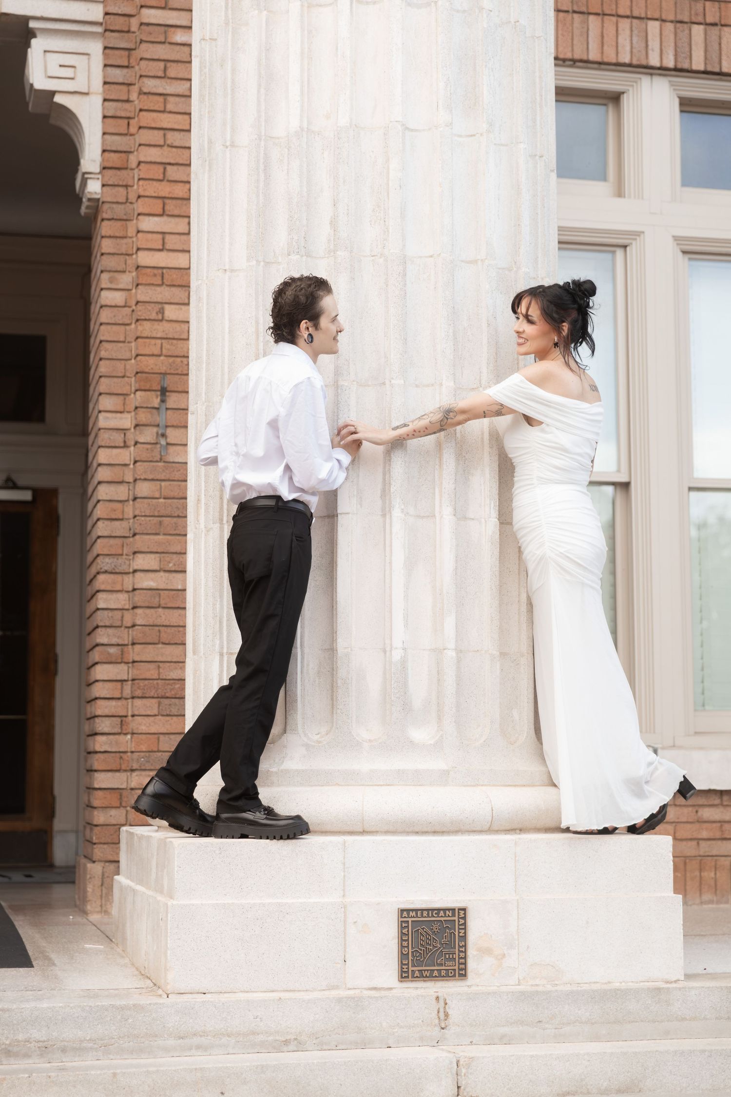 Bride and groom holding hands beside a stone column at a brick building on their wedding day.  Downtown Rome, GA